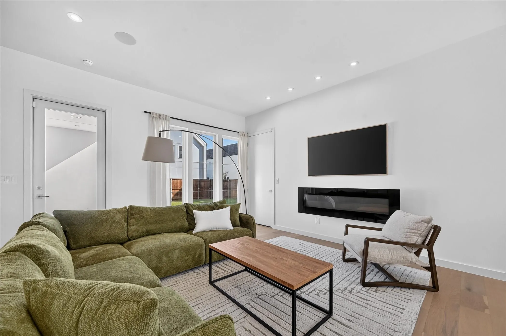 Modern living room featuring a curved olive-toned sectional sofa, wood-finish flooring, and neutral wall finishes