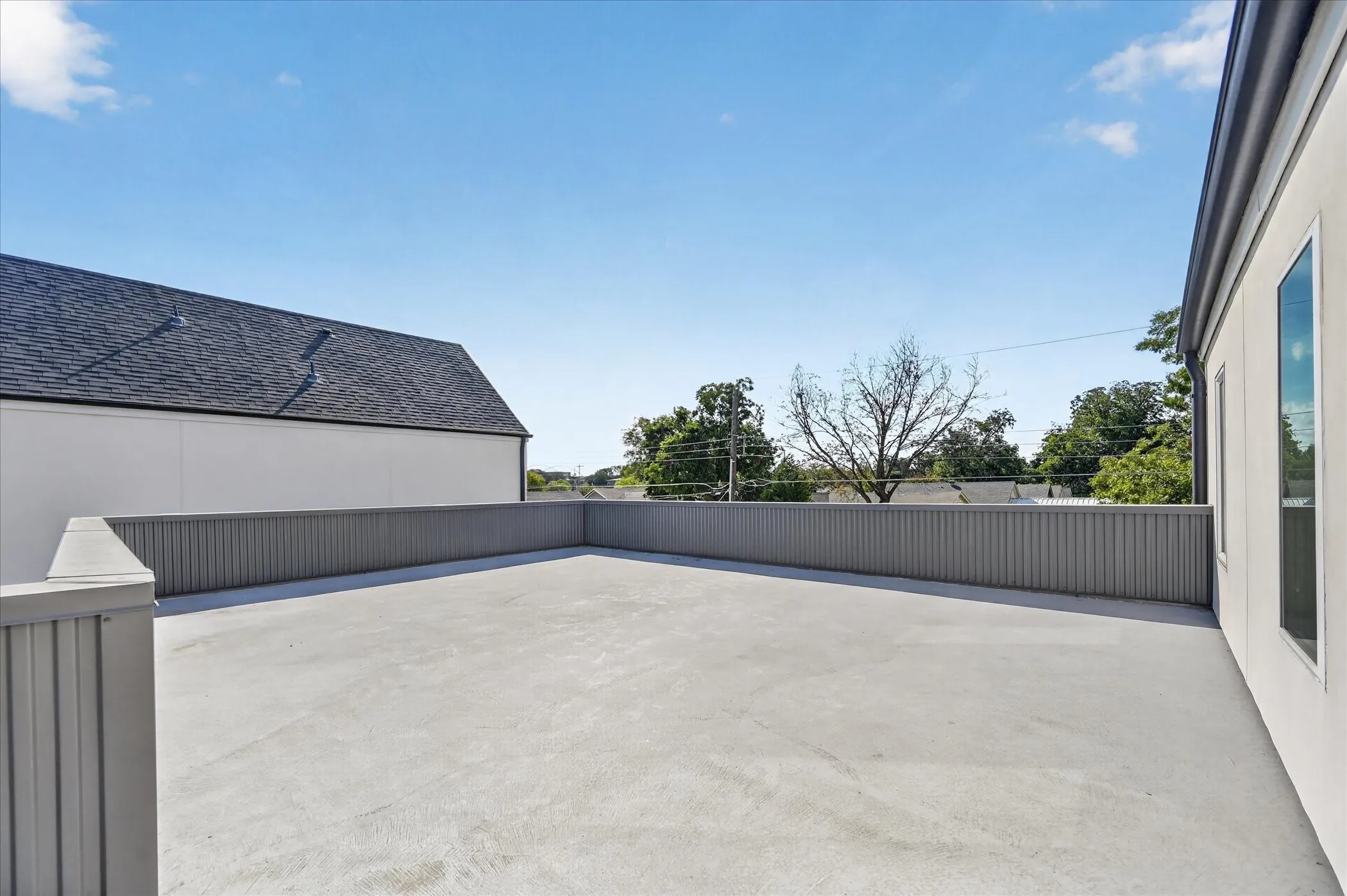 Expansive rooftop terrace with a durable concrete surface, full perimeter railing, and a windowed exterior wall