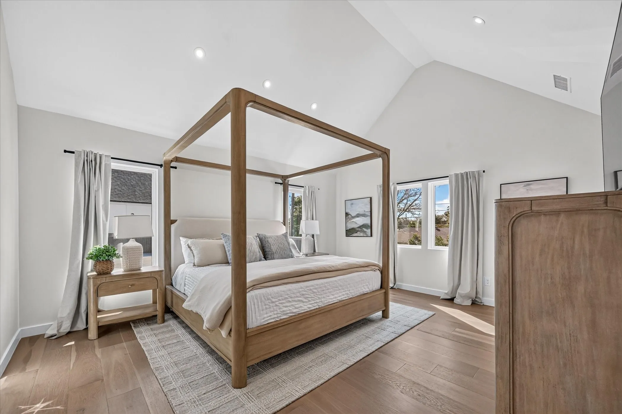 Primary Bedroom Suite featuring a wood-frame four-poster bed, hardwood flooring, vaulted ceiling with recessed lighting, and dual glass doors opening to natural light