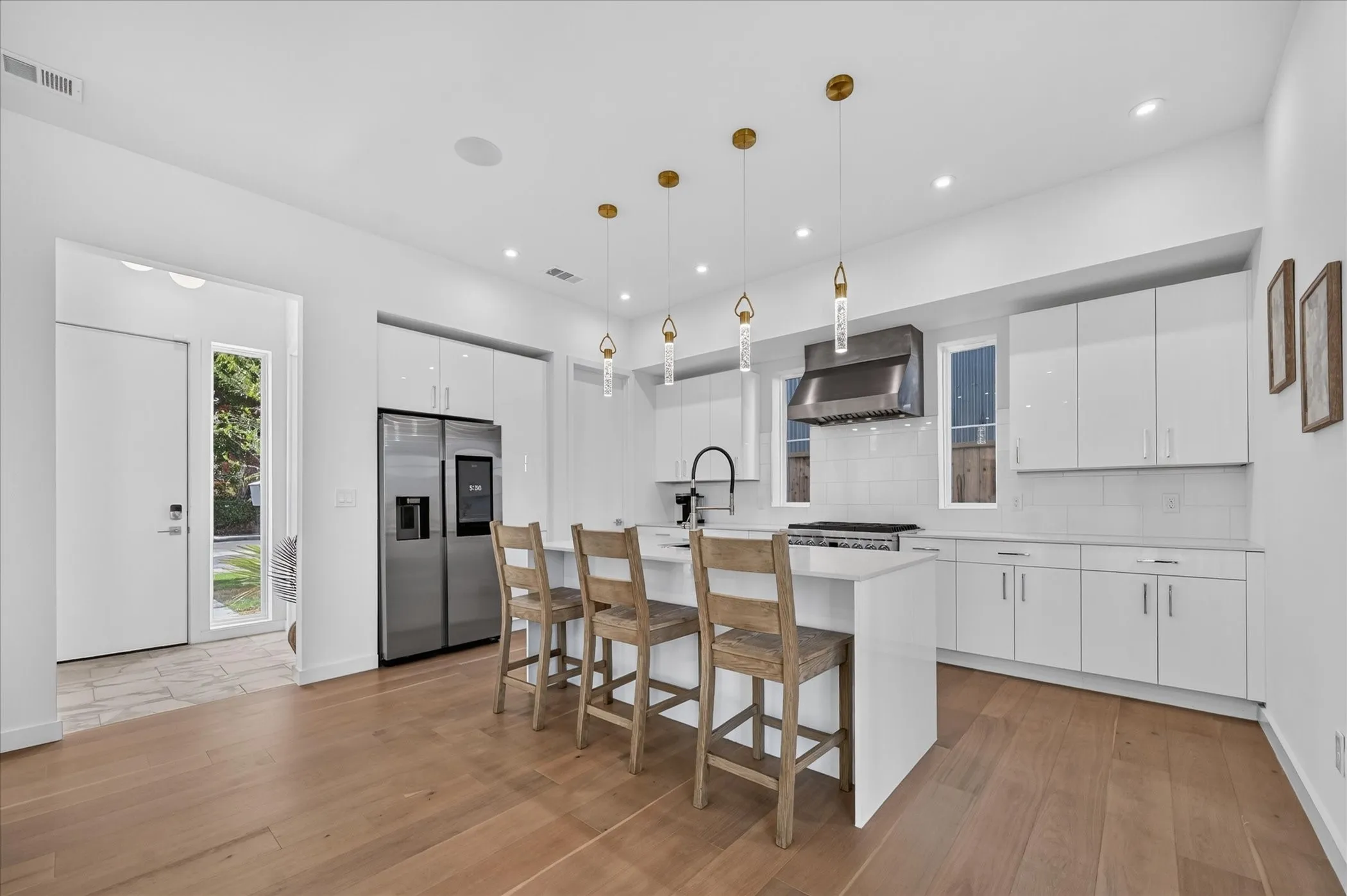 Open-concept kitchen with wood-finish flooring, white cabinetry, stainless steel appliances, and an island with pendant lighting