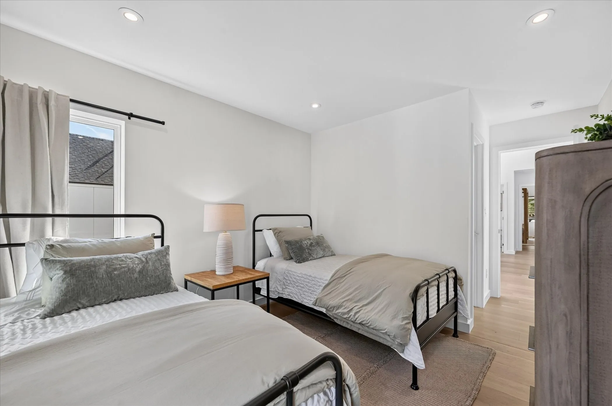 Recessed ceiling lighting, light wood-finish flooring, white walls, and a window with a black rod