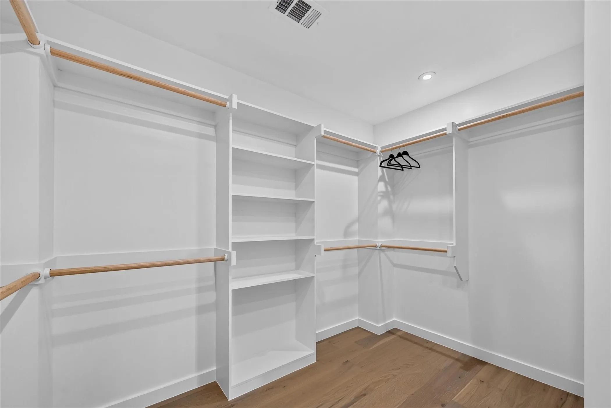 Spacious walk-in closet featuring custom built-in shelving and double hanging rods with wood-finish trim accents