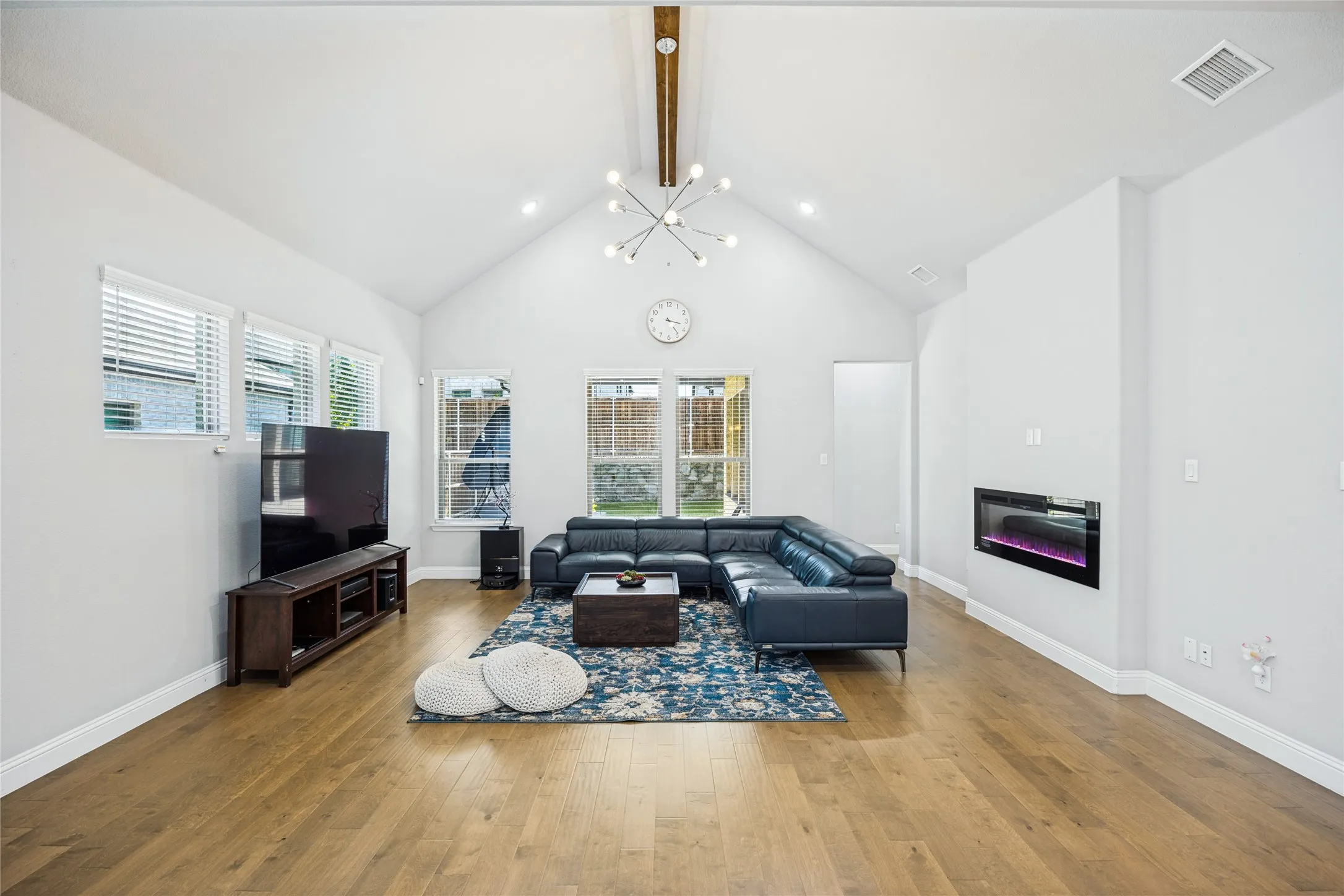 Vaulted ceilings, wood-finish flooring, multiple windows, built-in electric fireplace, and a modern chandelier
