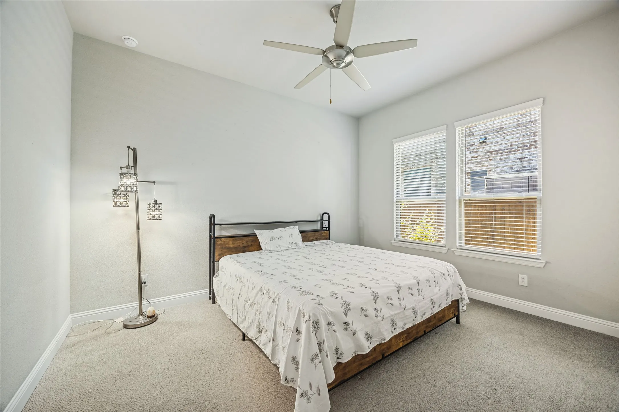 Vaulted ceiling with an attached ceiling fan, two windows with blinds, and light-toned carpeting
