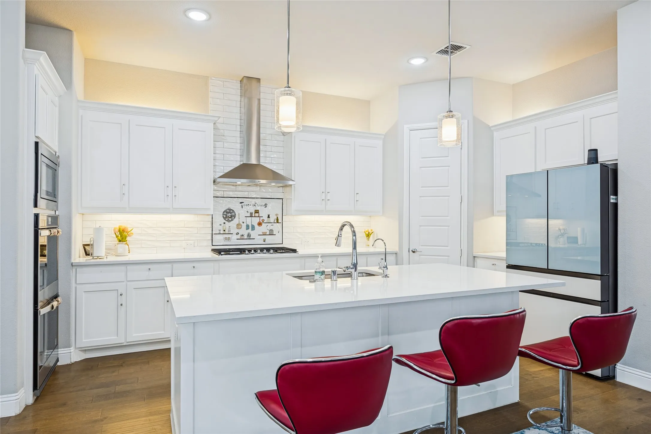 White cabinetry, recessed lighting, double wall ovens, a large kitchen island with an undermount sink, and wood-finish flooring