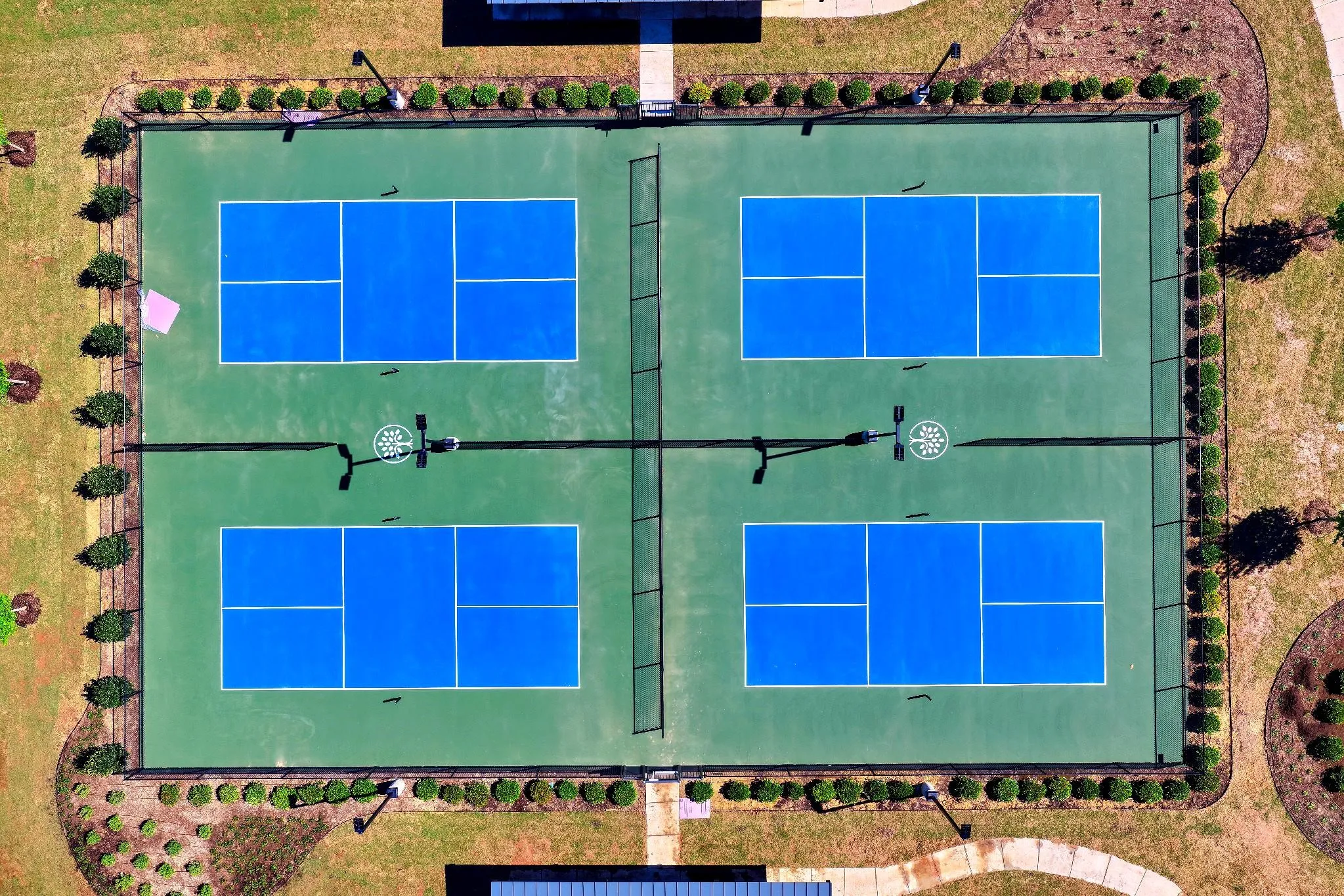 Four blue and green pickleball courts with perimeter fencing and landscaping