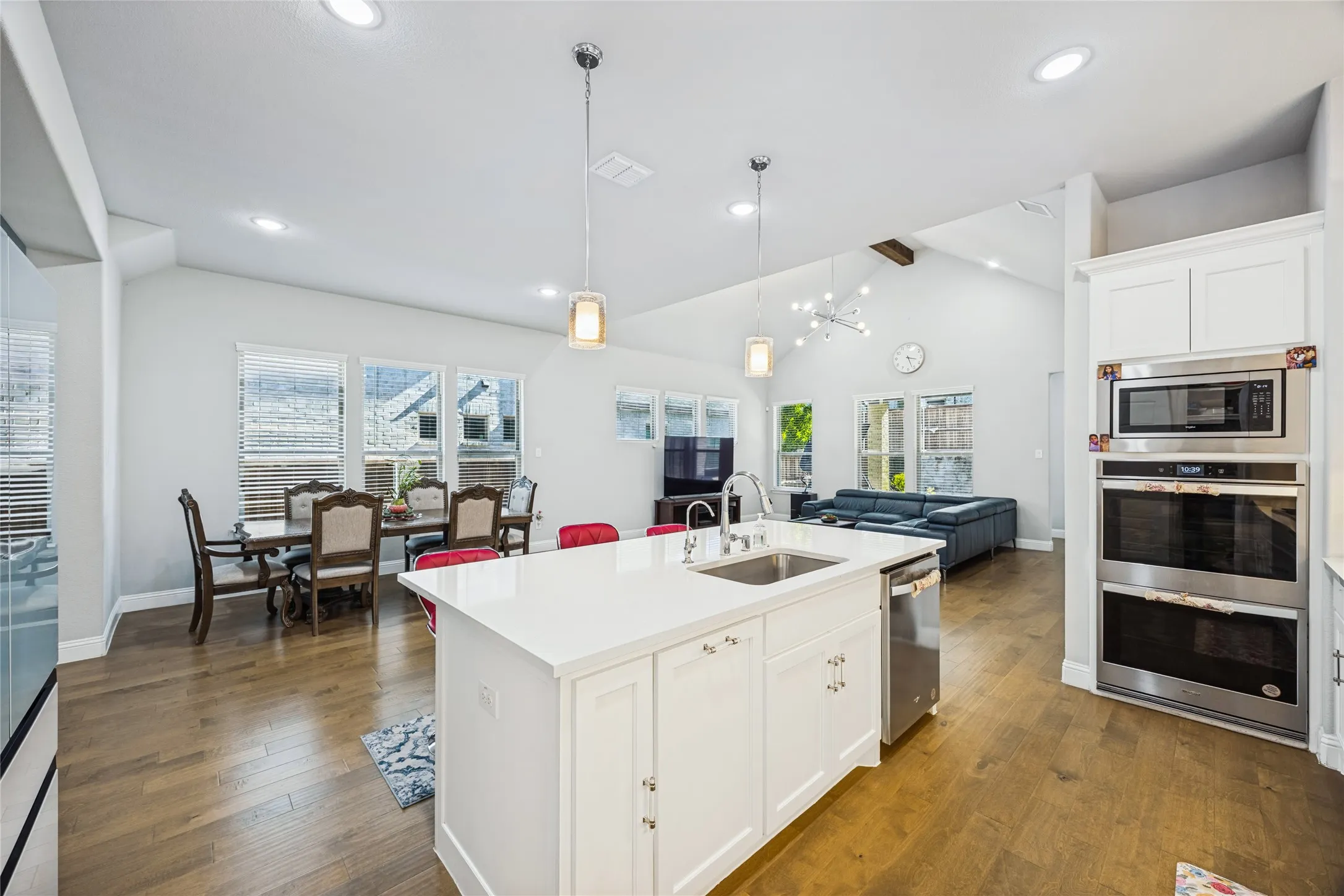 Kitchen island with integrated sink, stainless steel appliances, wood-finish flooring, vaulted ceiling, and recessed lighting