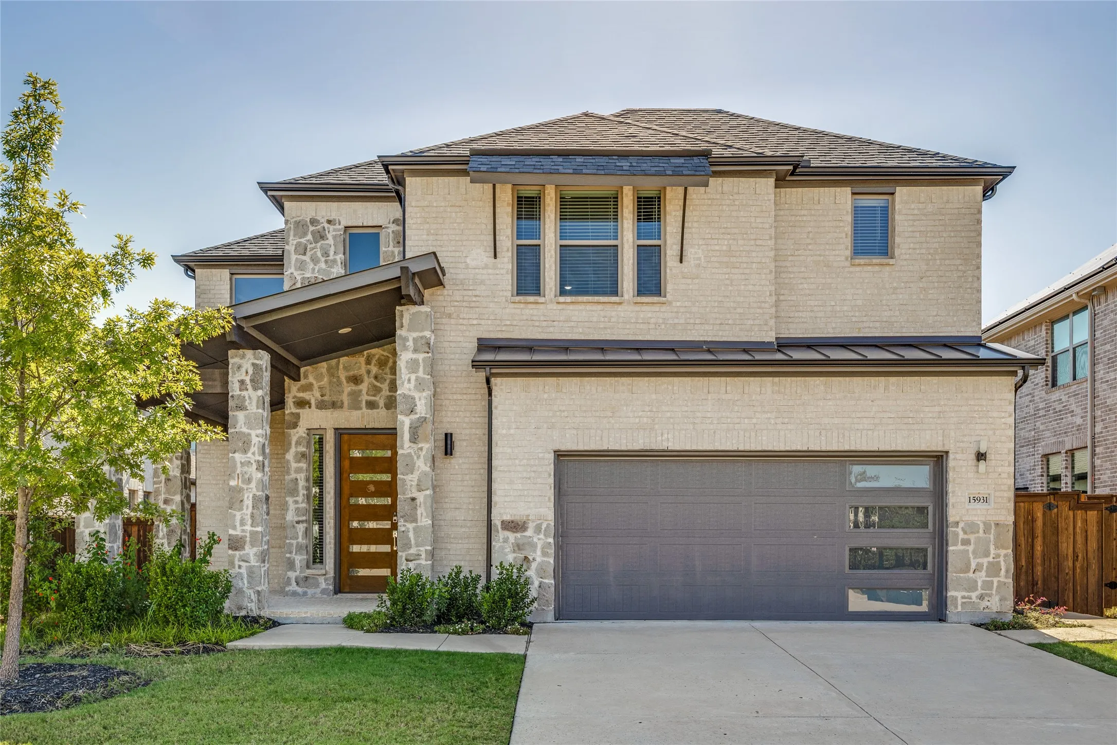 Contemporary exterior featuring light-colored brick, stone accents, a modern wood-finish entry door, a two-car garage with frosted glass panels, and an extended covered porch