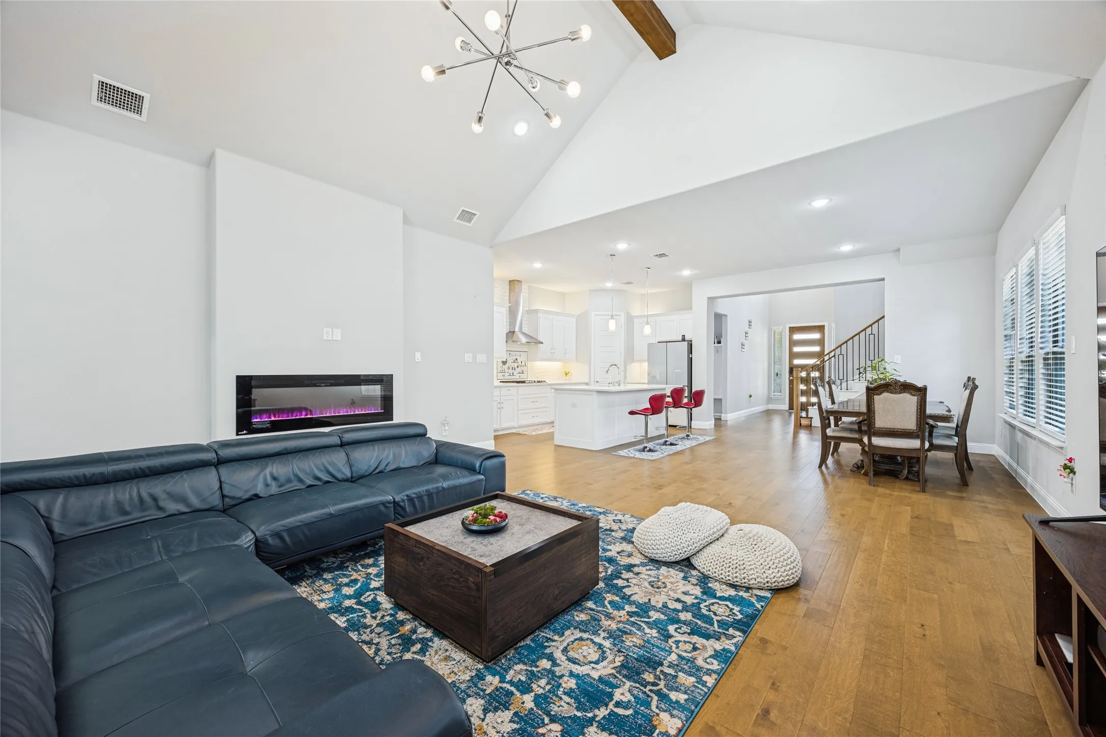 Vaulted ceilings with an exposed wood beam, contemporary chandelier, wood-finish flooring, and a modern linear fireplace