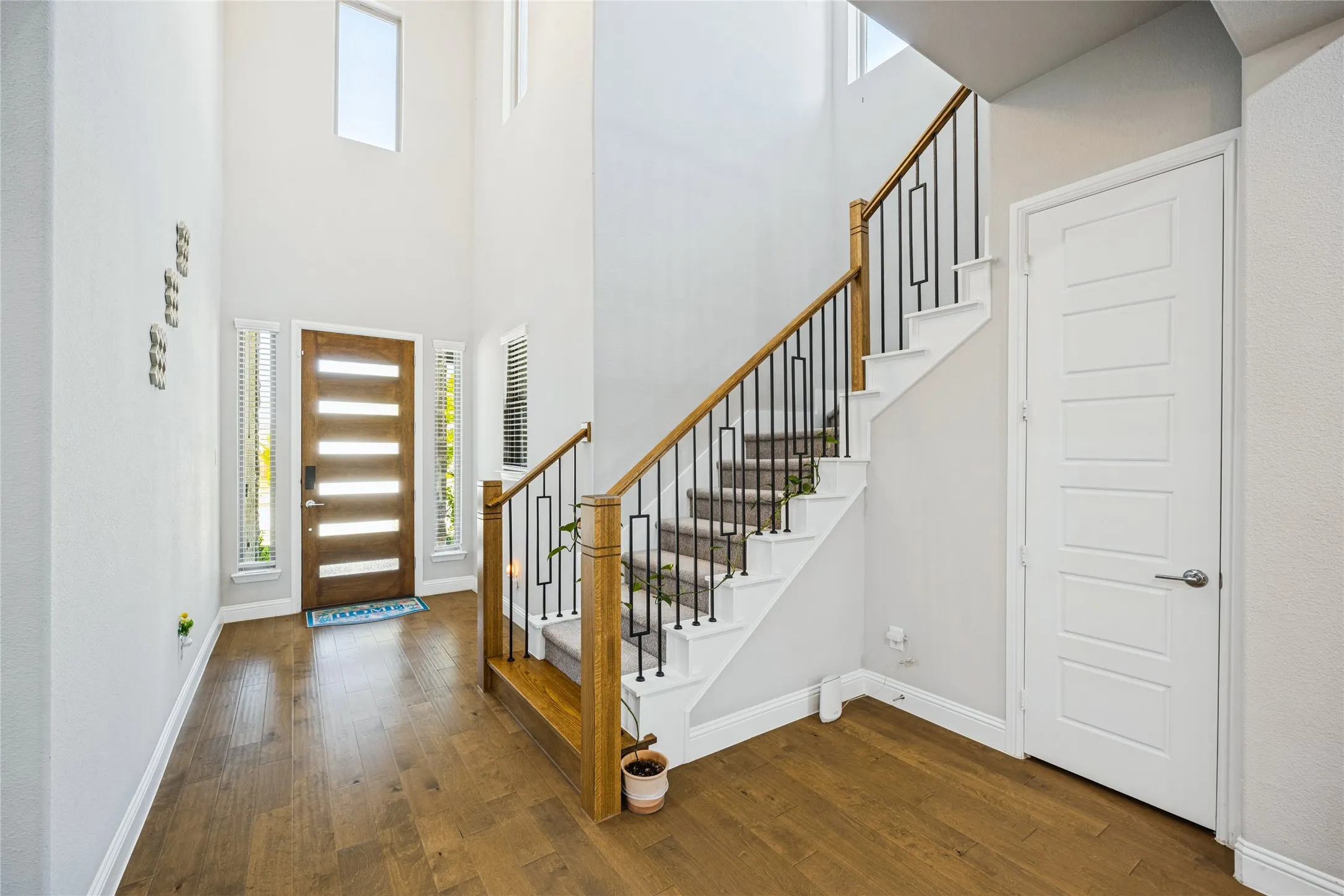 Two-story foyer with wood-finish flooring, a contemporary wood-panel entry door, and a staircase featuring wood handrails and wrought iron balusters