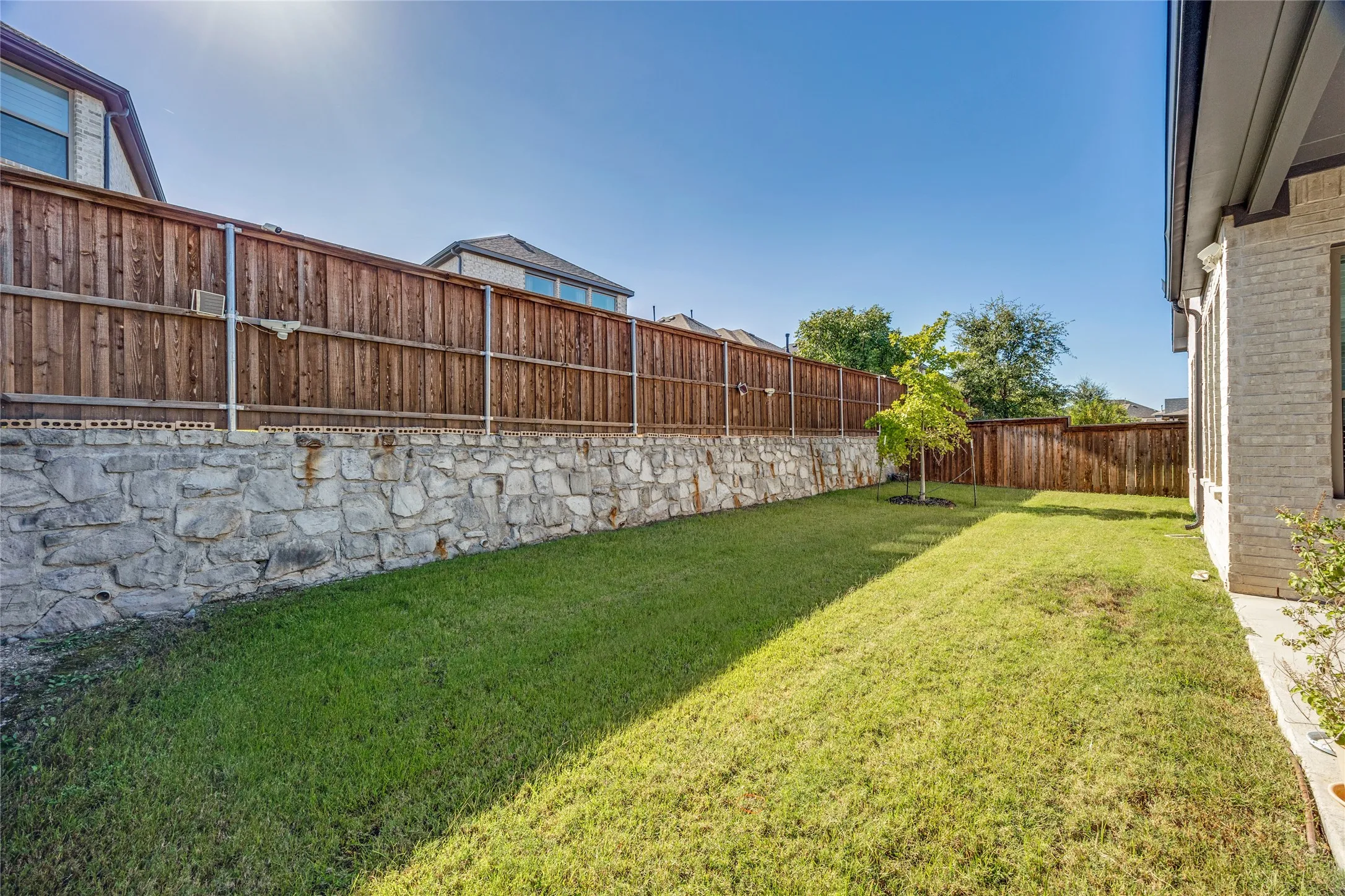 Expansive lawn area with a stone retaining wall and full wood privacy fencing