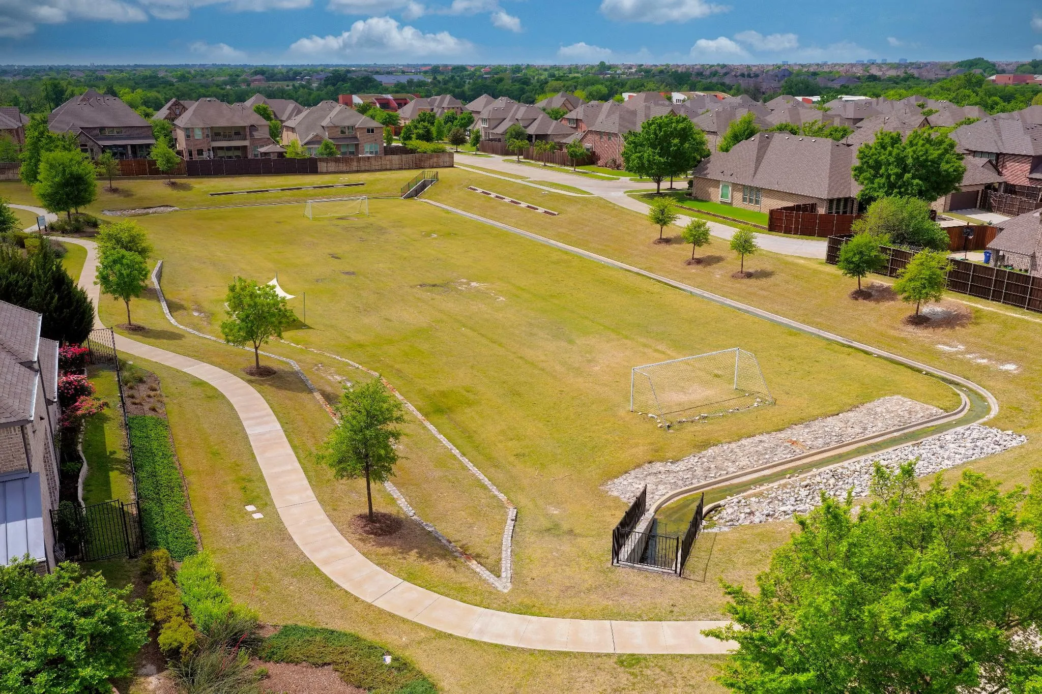 Expansive green space featuring a walking path, mature trees, and sports goals