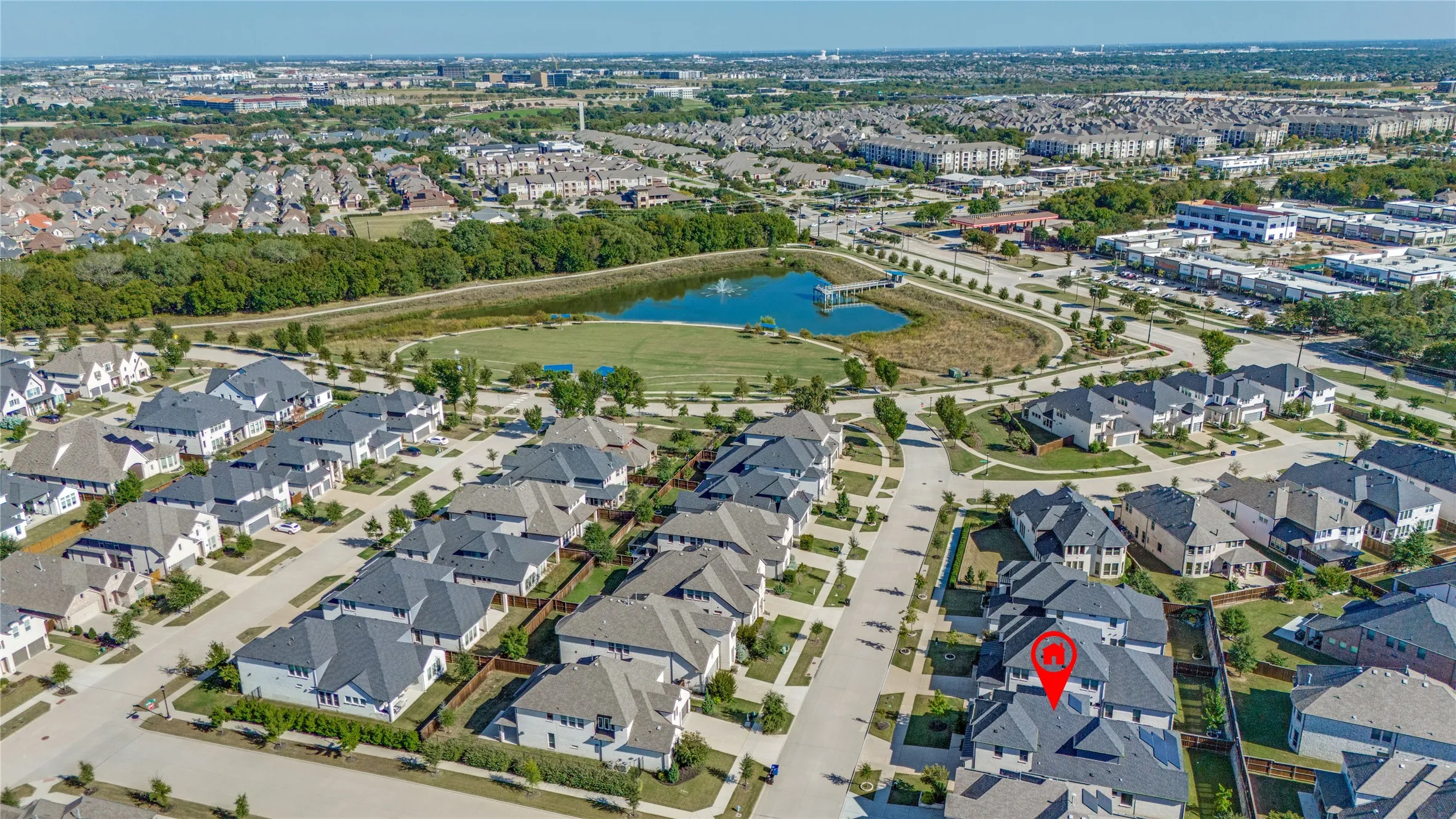 Aerial perspective of a suburban community featuring a prominent pond, surrounding green space, and residential properties with dark-pitched roofs