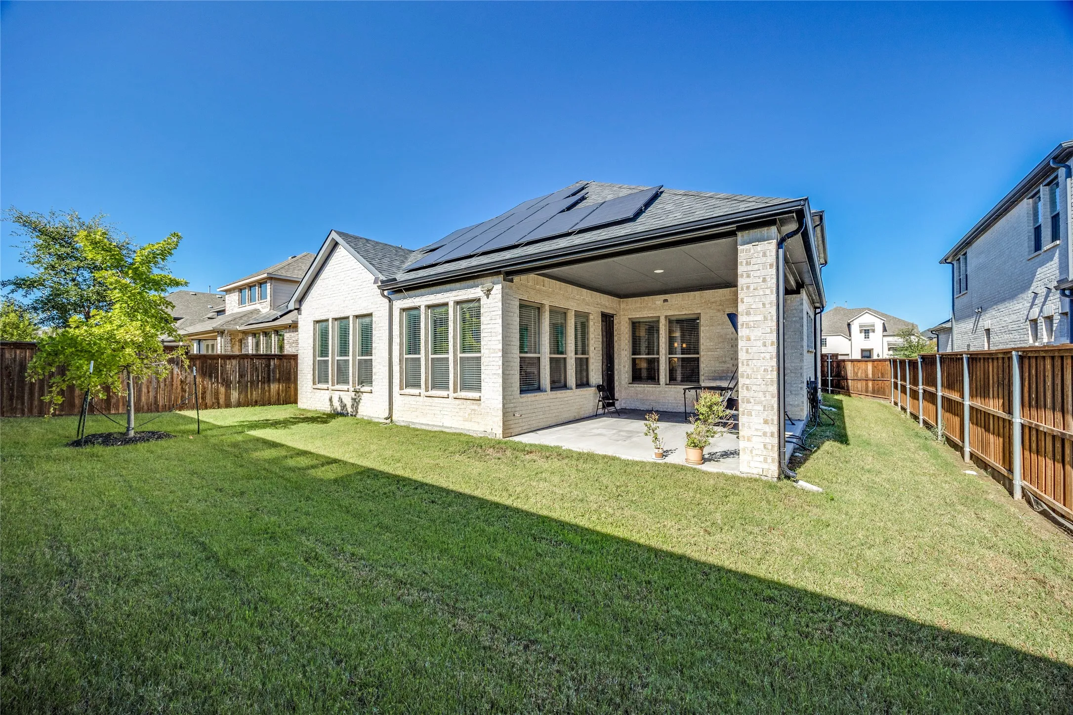 Expansive backyard featuring a covered patio, solar panels, and a wood privacy fence
