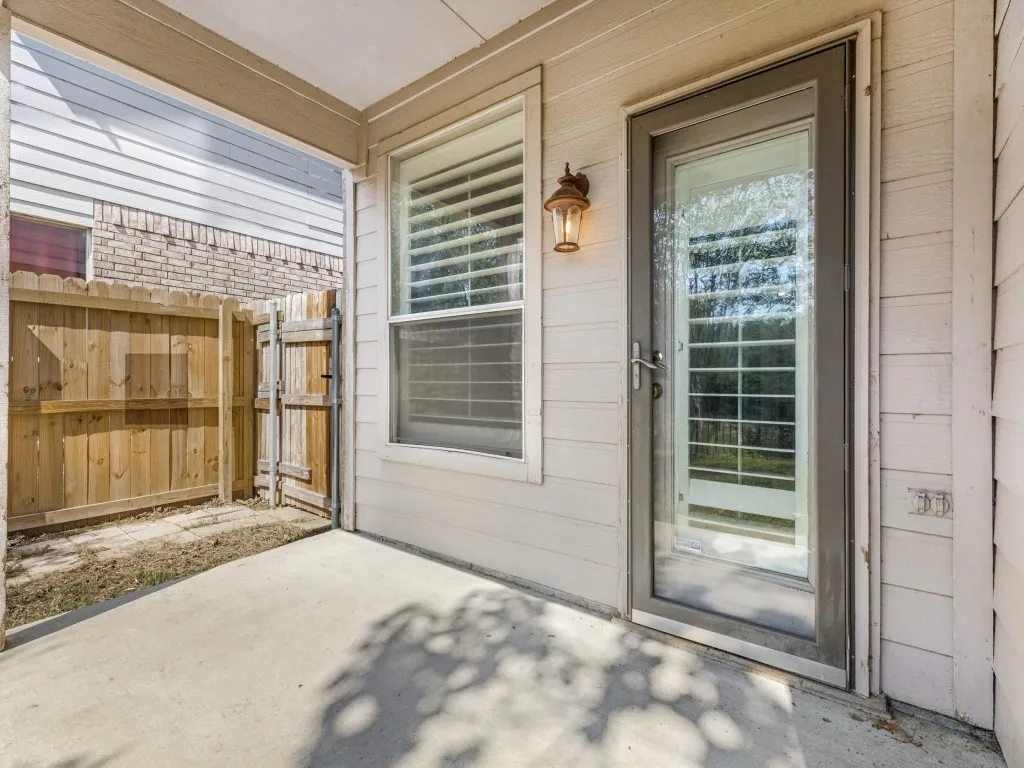 Covered patio with concrete flooring, wood privacy fencing, and an exterior wall light fixture