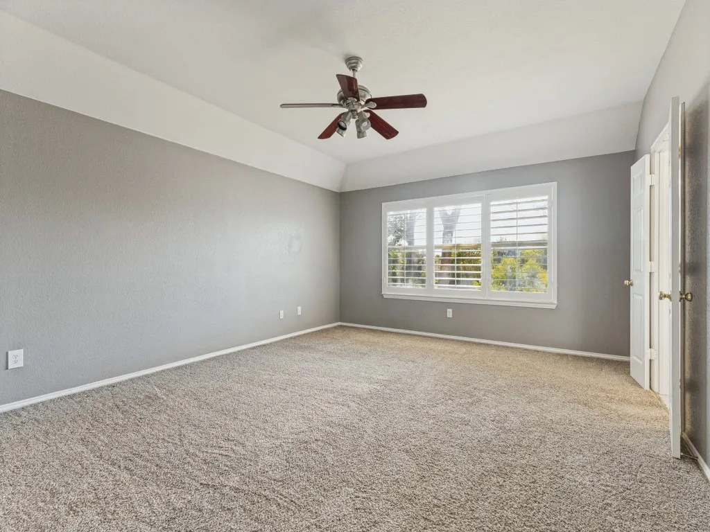 Tray ceiling with a ceiling fan, light-colored carpeting, large window with plantation shutters, and a paneled interior door