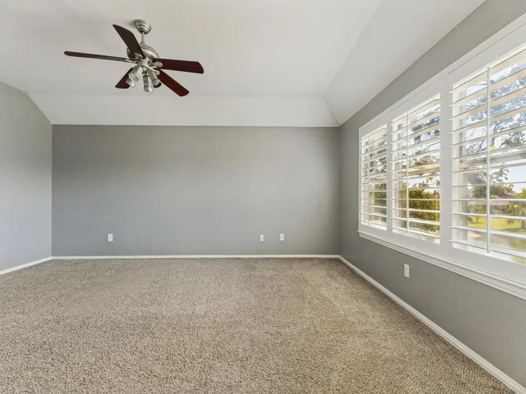 Expansive room featuring plush carpeting, a multi-pane window with plantation shutters, a ceiling fan with integrated lighting, and a tray ceiling