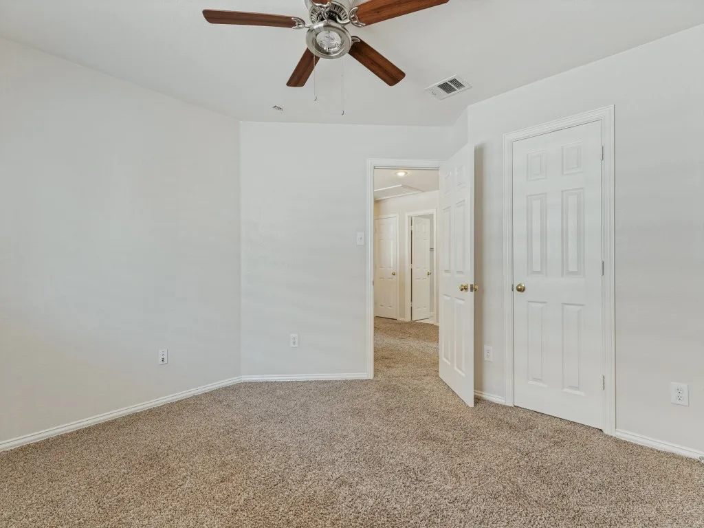 Plush carpeting, neutral wall finishes, and a ceiling fan with wood-finish blades