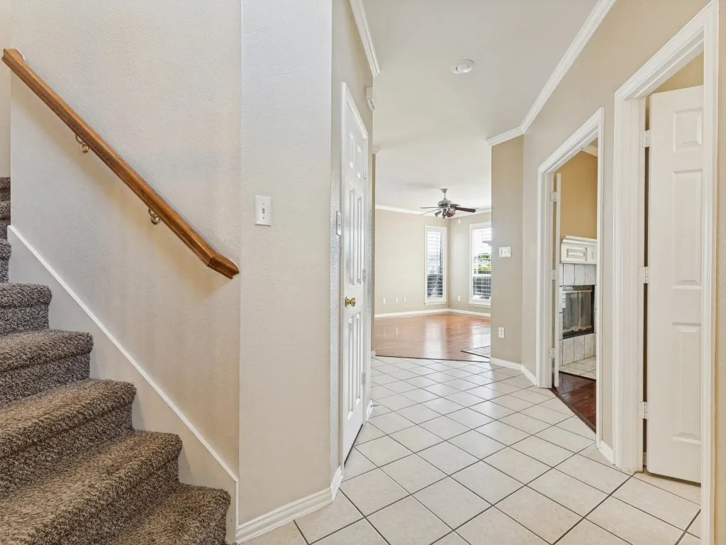 Tiled flooring in the entryway with a plush carpeted staircase featuring a wood handrail