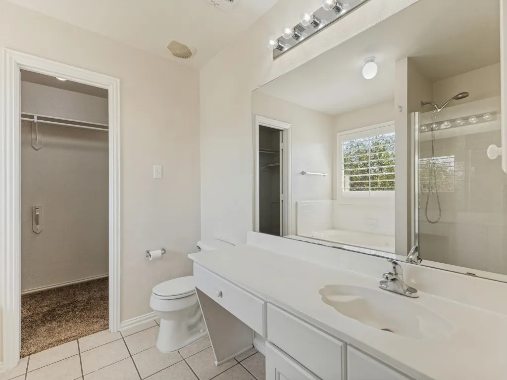 White tiled flooring, vanity with integrated sink, walk-in shower with clear glass enclosure, built-in bathtub, and window with privacy blinds