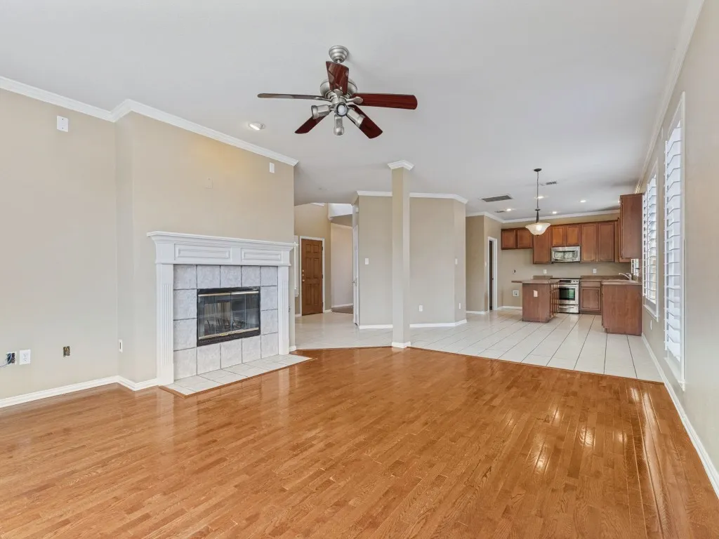 Wood-finish flooring, white fireplace with tile surround, ceiling fan, crown molding, and plantation shutters