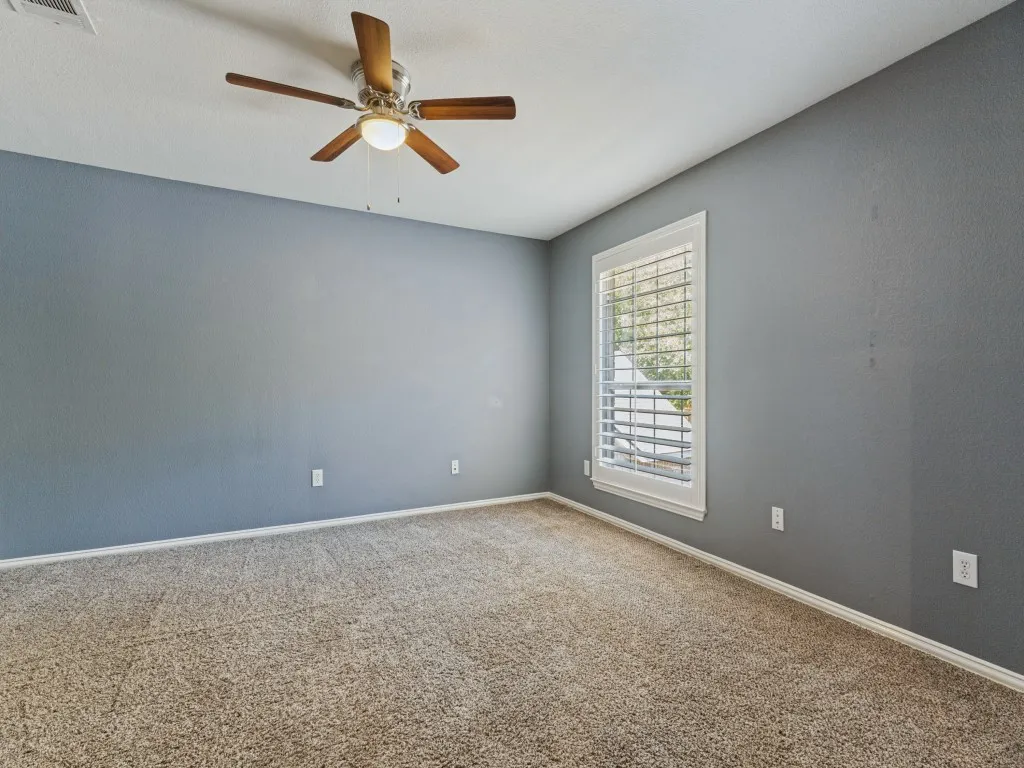 Neutral-toned carpeting, ceiling fan with wood-finish blades, and white plantation shutters on the window