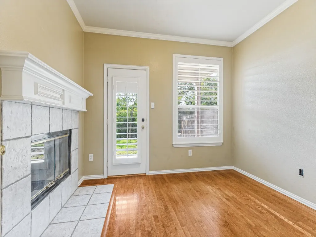 Hardwood flooring, tiled fireplace with mantel, window with plantation shutters, crown molding, and a glass-paneled door