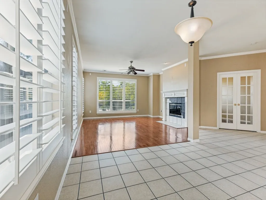 Spacious interior featuring a decorative fireplace, large windows with plantation shutters, wood-finish flooring, and white French doors