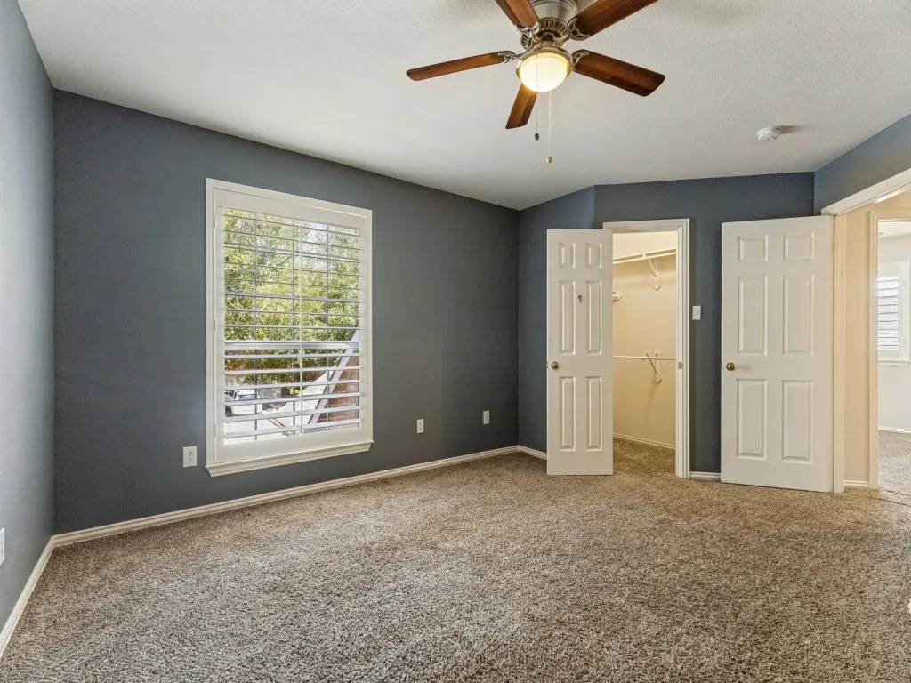 Spacious room featuring neutral carpeting, a ceiling fan with integrated lighting, and a window with plantation shutters