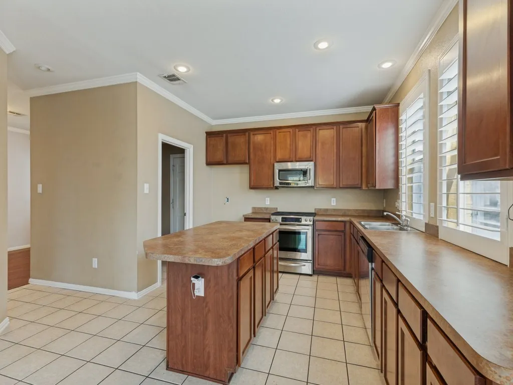Kitchen featuring a central island, stainless steel appliances, wood-finish cabinetry, neutral countertops, and tile flooring
