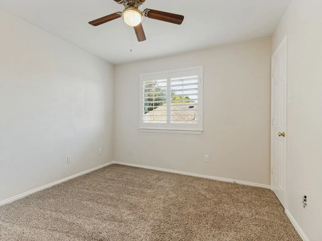 Window with white plantation shutters, ceiling fan with light fixture, light-colored walls, and neutral carpet flooring