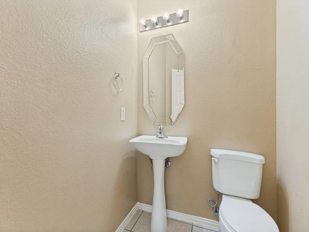 Pedestal sink with chrome faucet, octagonal framed mirror, and a four-light vanity fixture