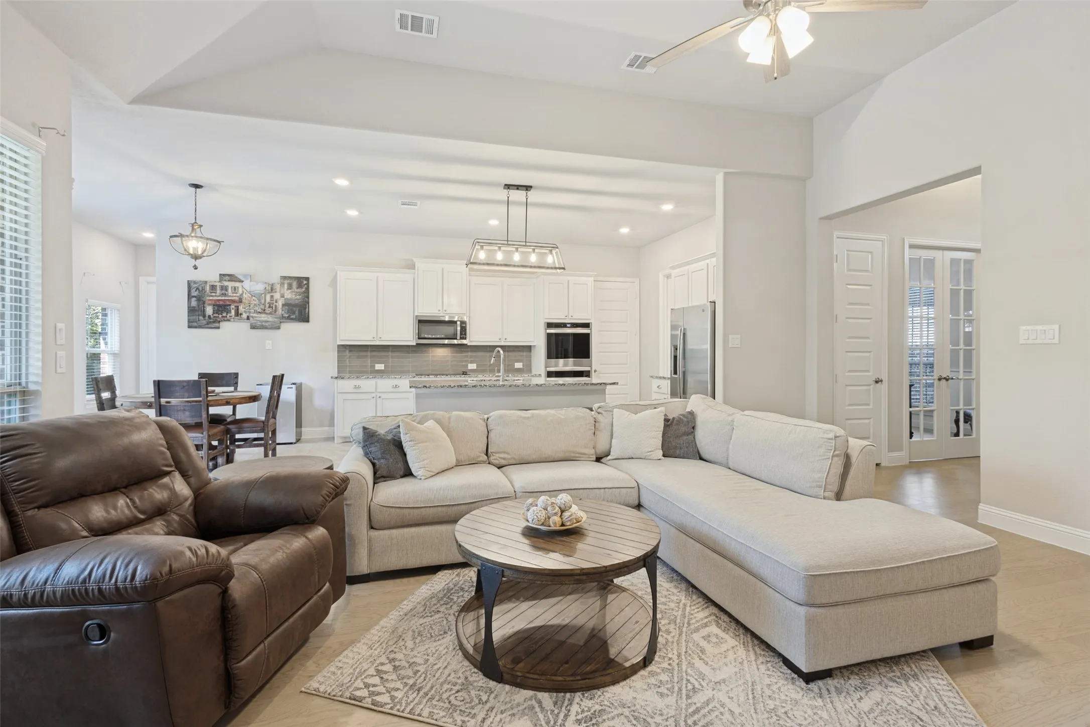 Vaulted ceiling with ceiling fan, recessed lighting, white cabinetry, stainless steel appliances, and French doors