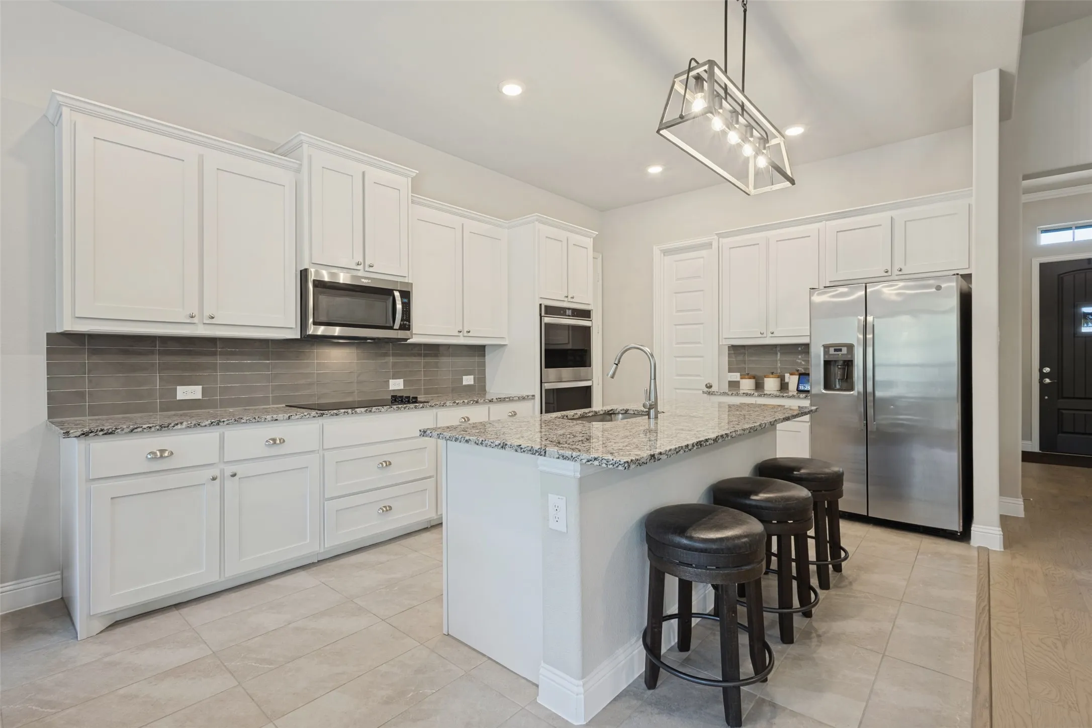 Contemporary kitchen featuring white cabinetry, granite countertops, a tile backsplash, and stainless steel appliances