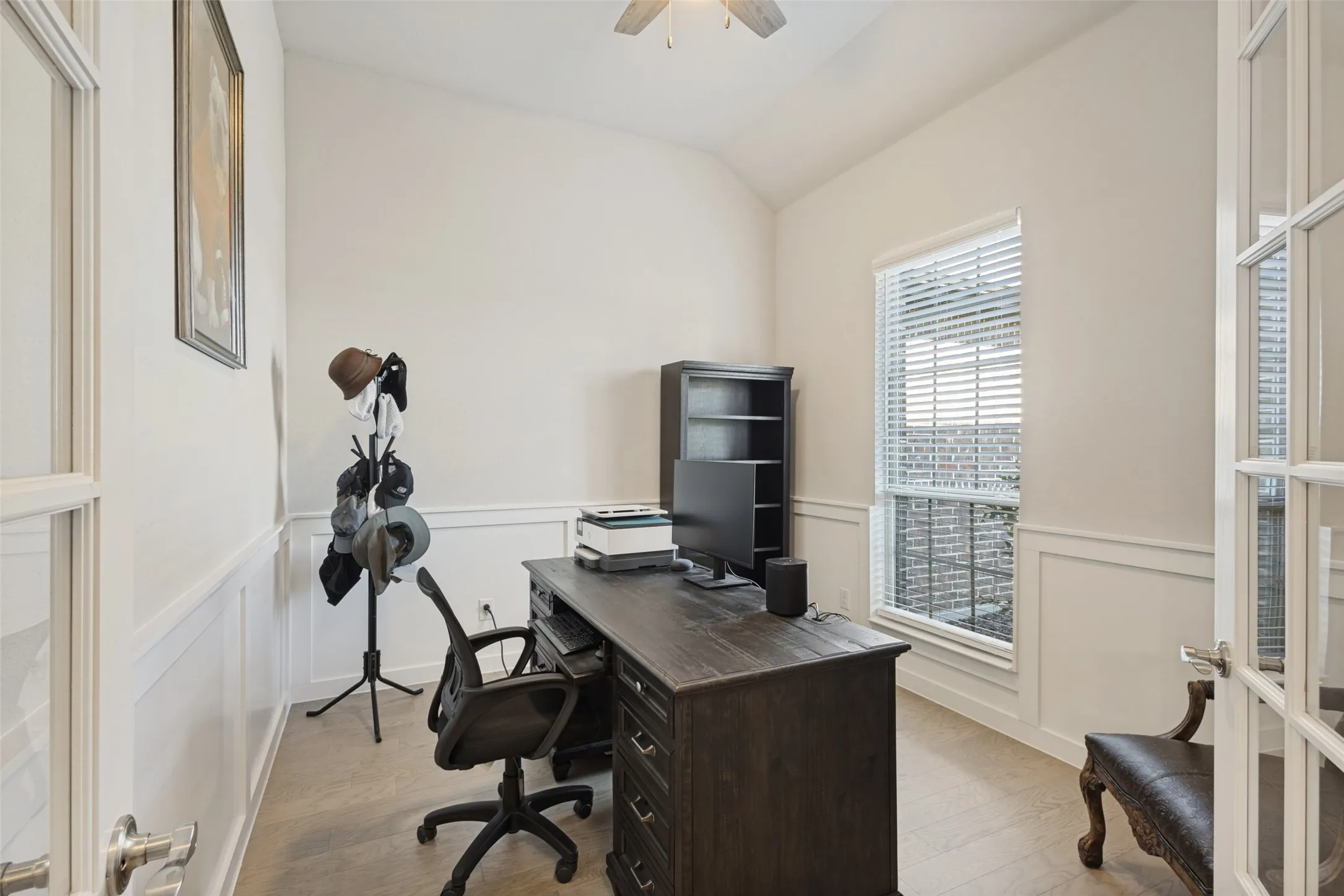 Vaulted ceiling, paneled accent walls, French doors, ceiling fan, and wood-finish flooring