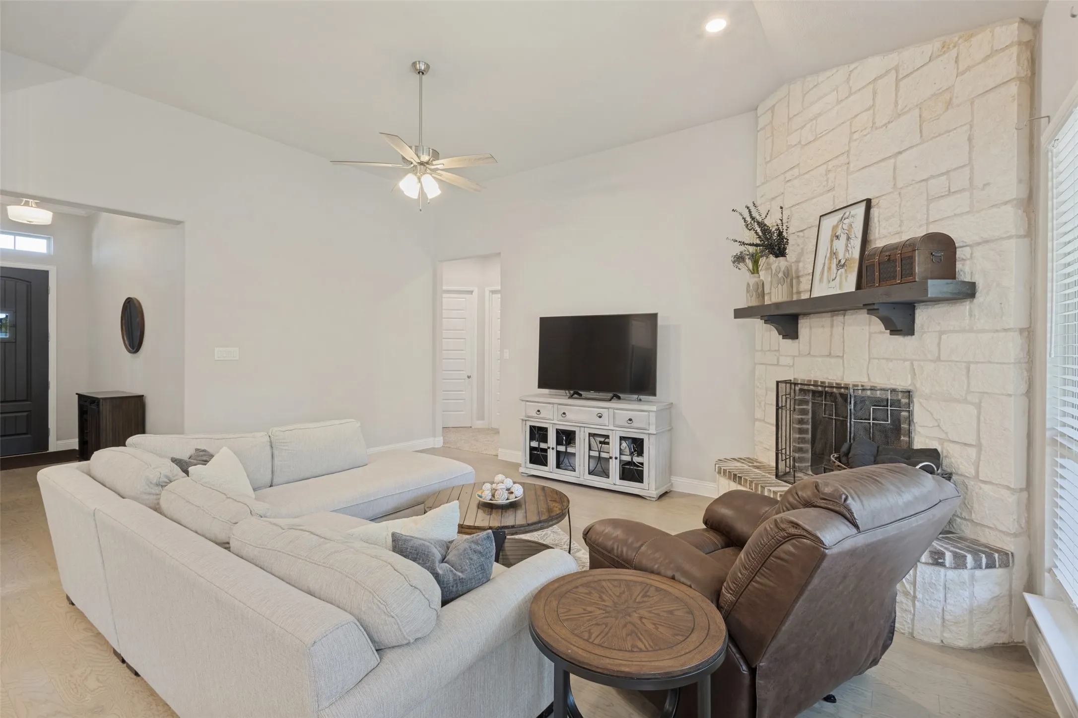 Vaulted ceilings with recessed lighting, stone-clad fireplace, wood-finish flooring, and a ceiling fan