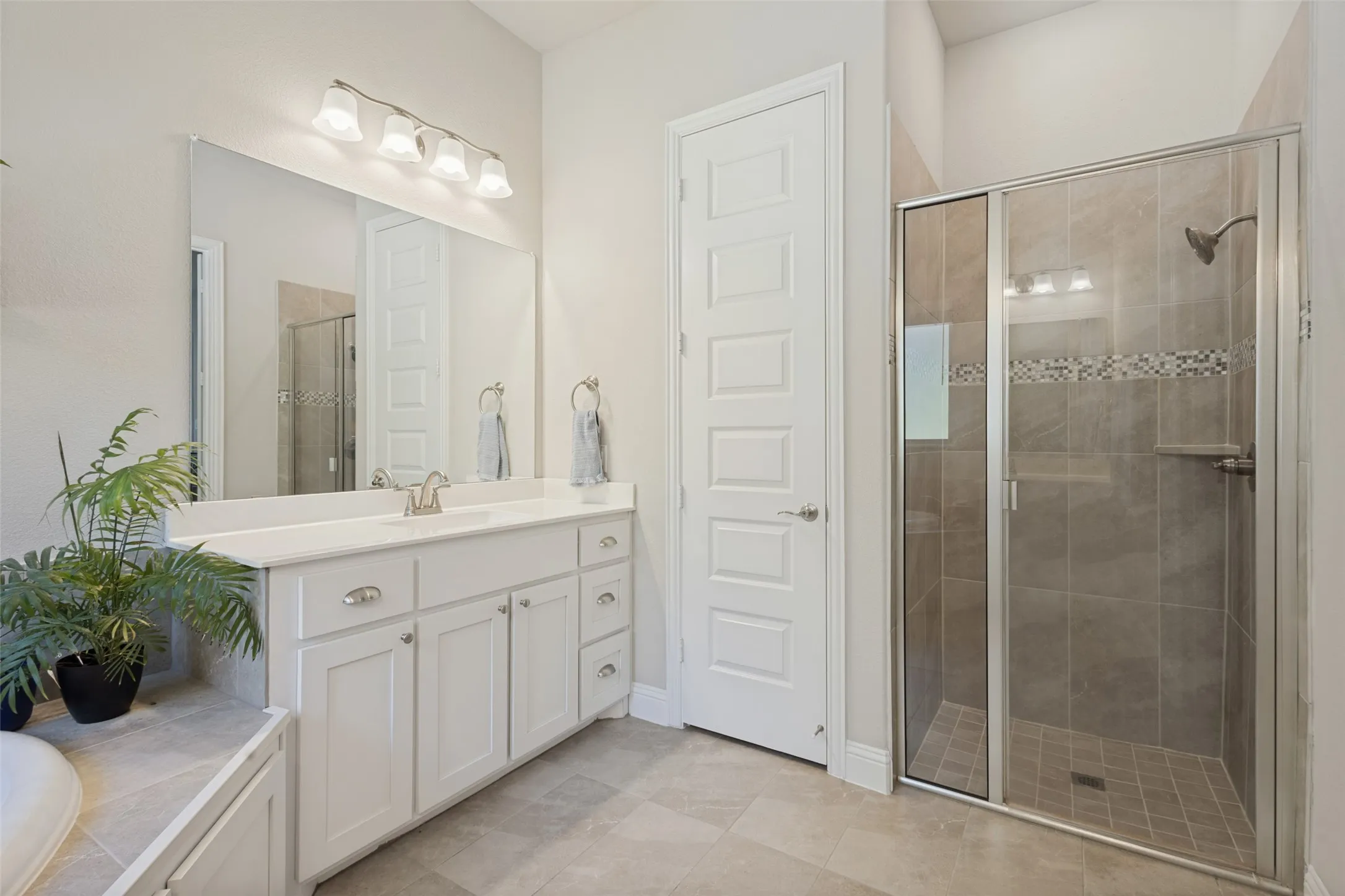 Walk-in shower with tile surround and glass enclosure, white vanity with integrated sink and chrome fixtures, large wall-mounted mirror, and tile flooring
