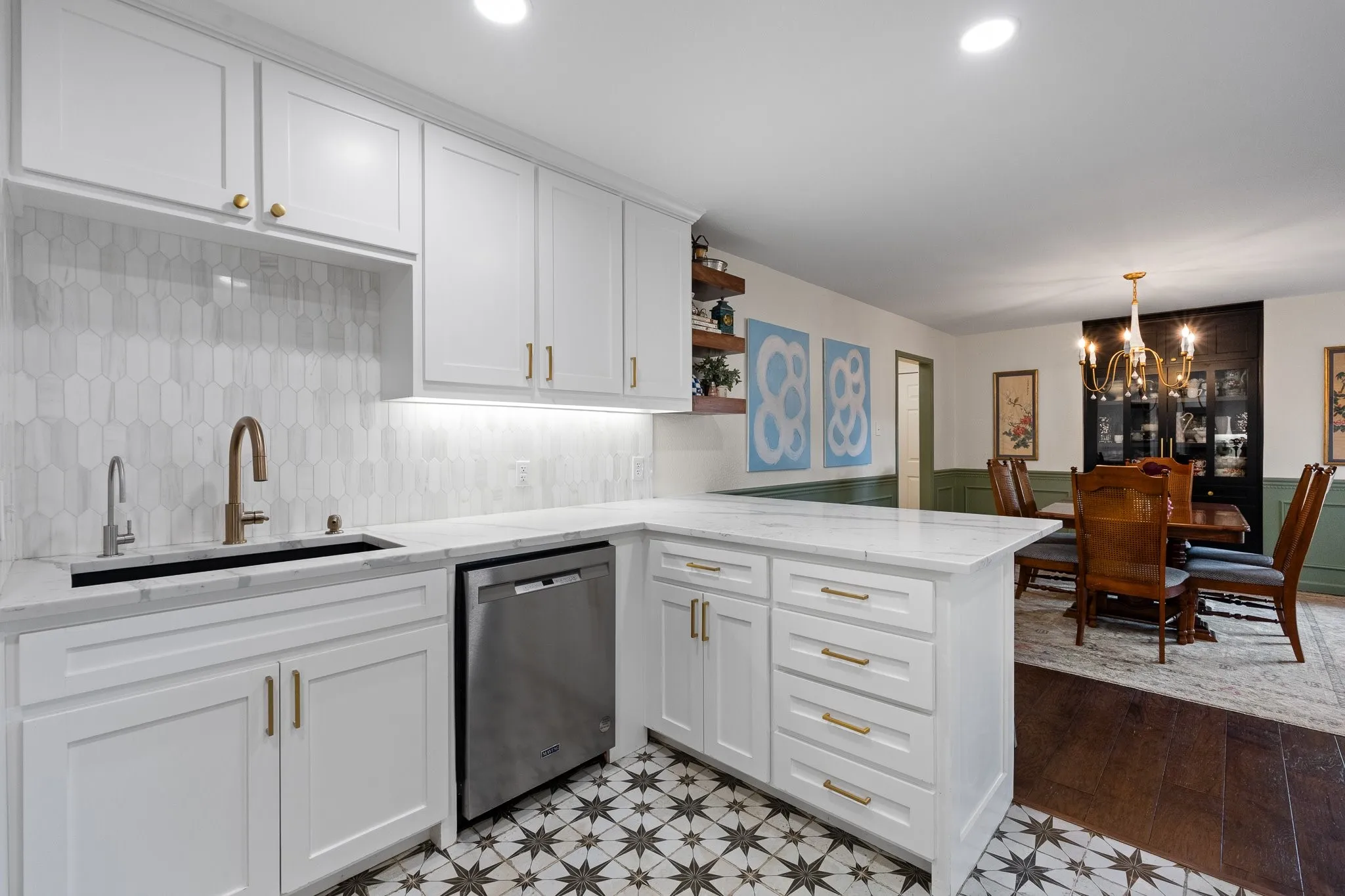 White shaker cabinetry with gold-tone hardware, a stainless steel dishwasher, a single basin sink with a bronze-tone faucet, and designer tile