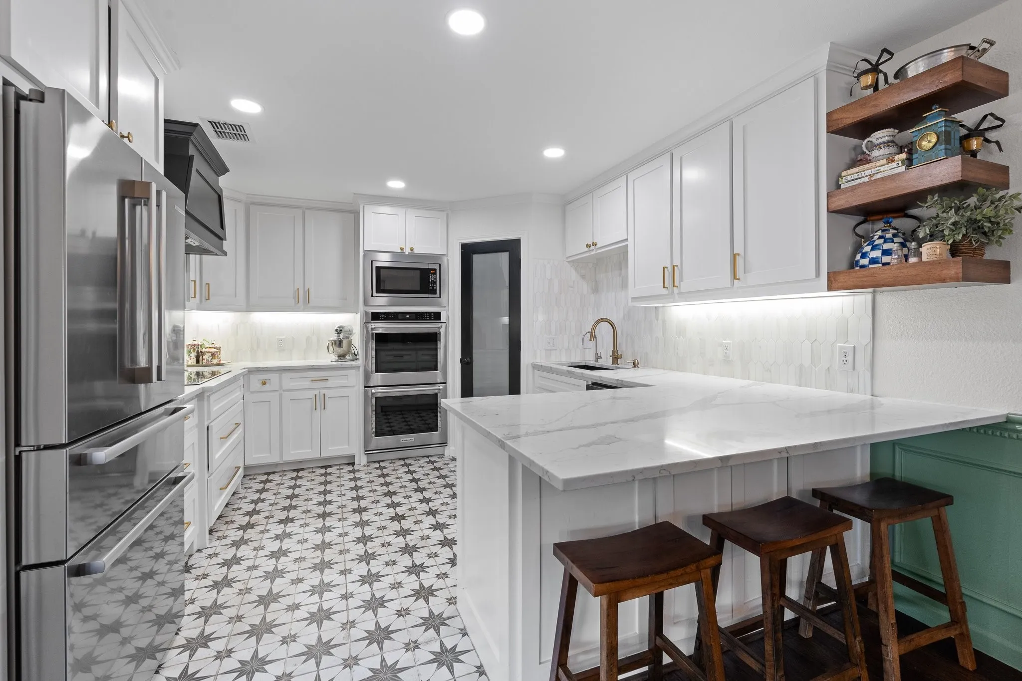 Kitchen featuring white cabinetry, stainless steel appliances, designer tile, under-cabinet lighting, and a peninsula with seating and additional storage cabinets