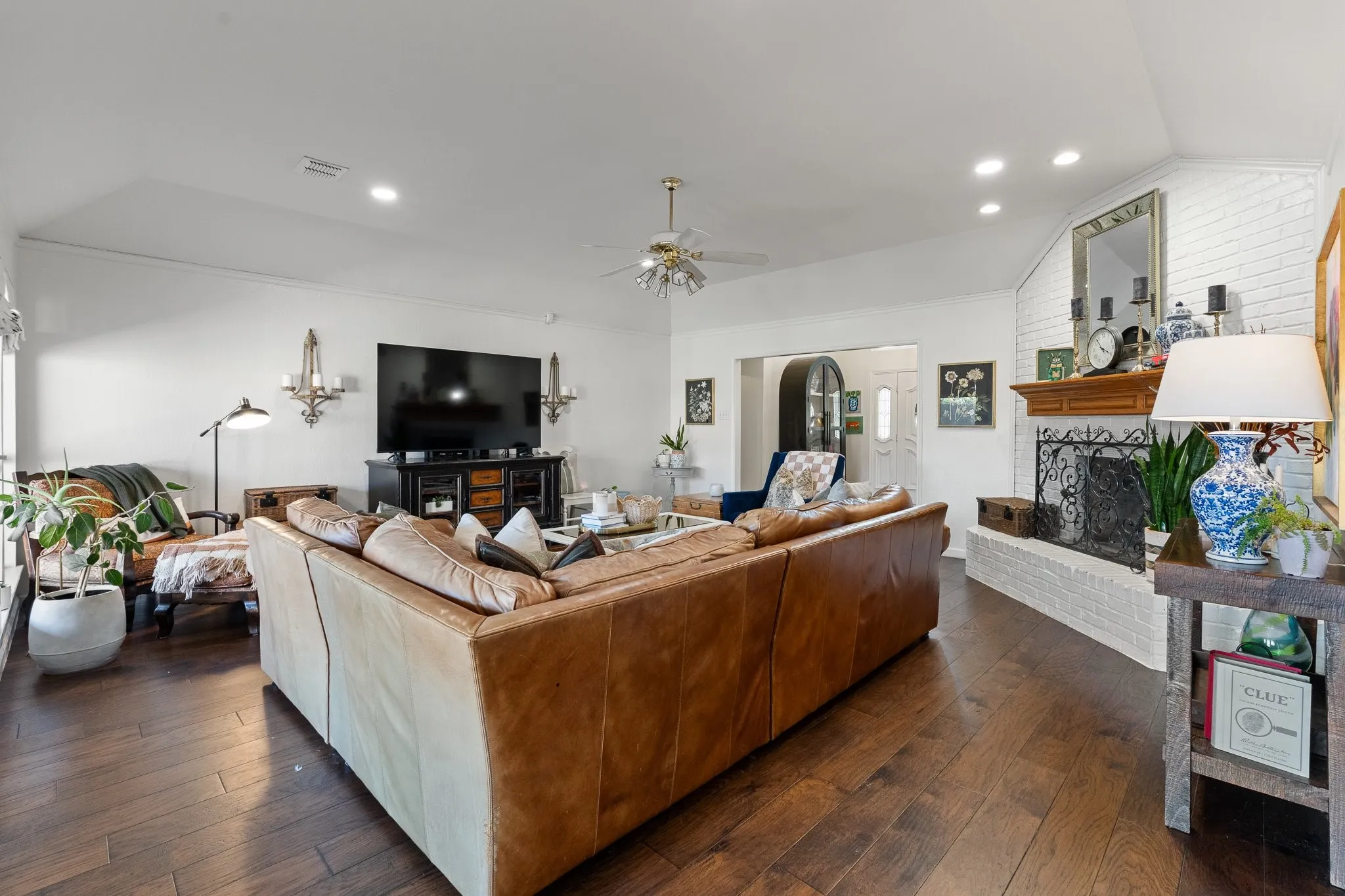 Spacious living area featuring wood flooring, a white brick fireplace with a wood mantel, vaulted ceilings, and recessed lighting