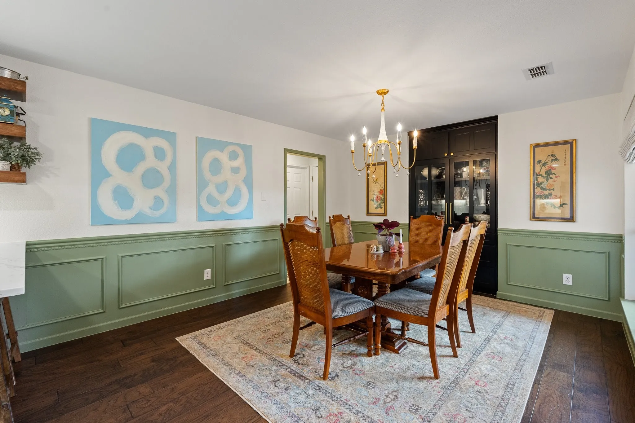 Wood flooring, accent wainscoting, built-in cabinetry with glass paneling, and an overhead chandelier with candle-style lights