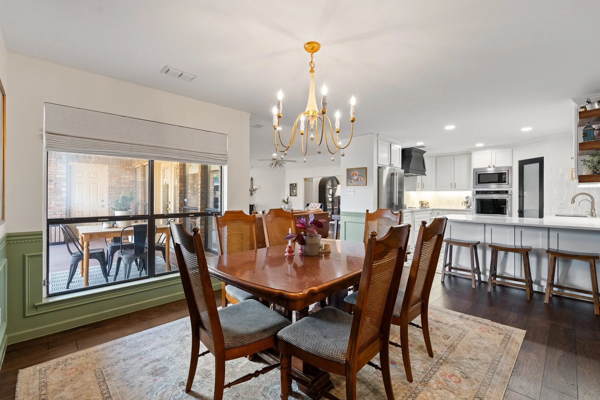 Wood flooring, a gold-tone chandelier, and a large window with a Roman shade