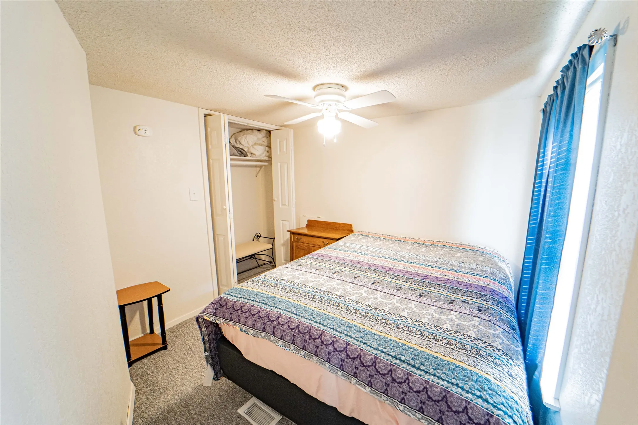 White walls, textured ceiling, ceiling fan with light fixture, carpeted flooring, and a window