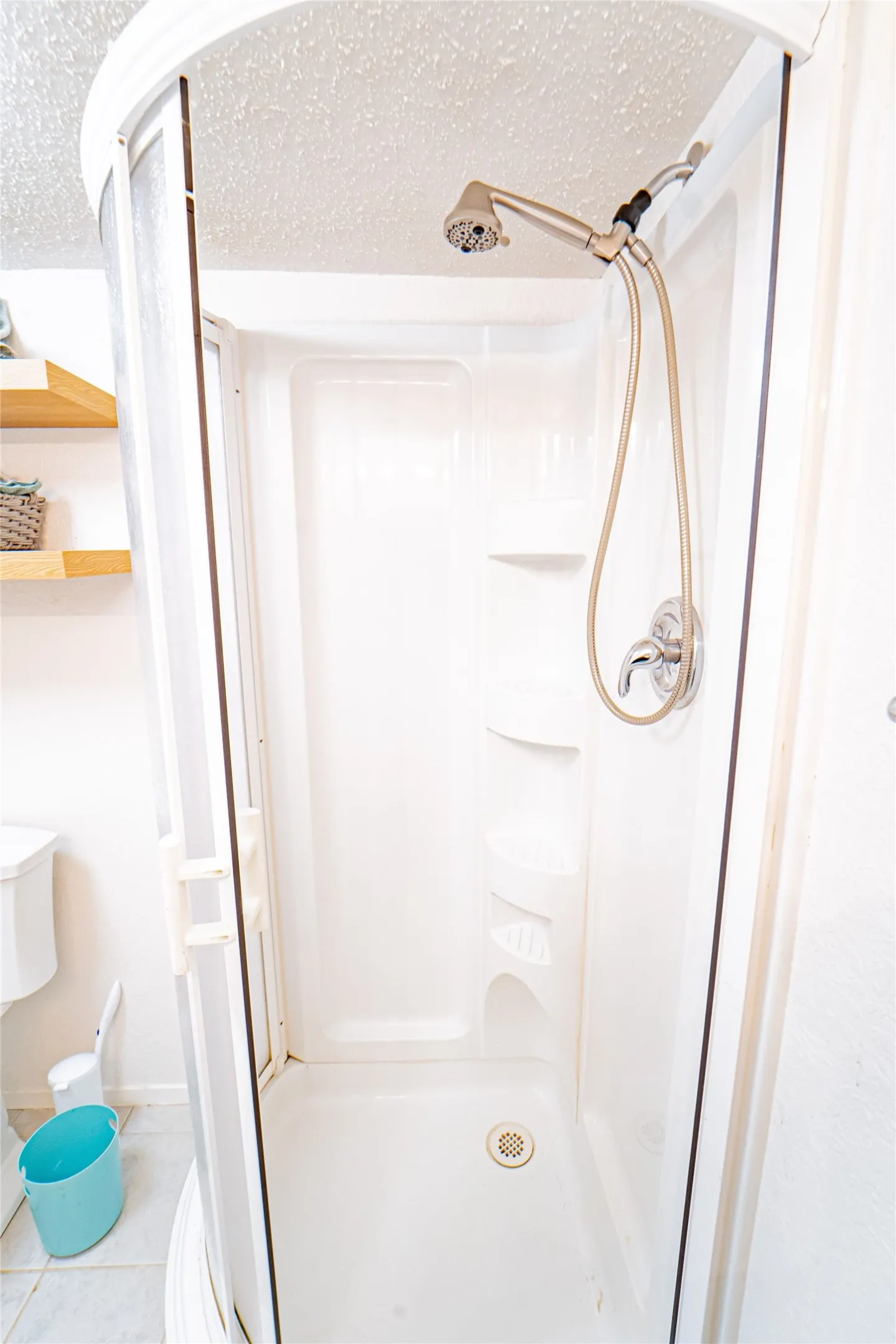 Enclosed shower stall with a brushed nickel showerhead and built-in shelving