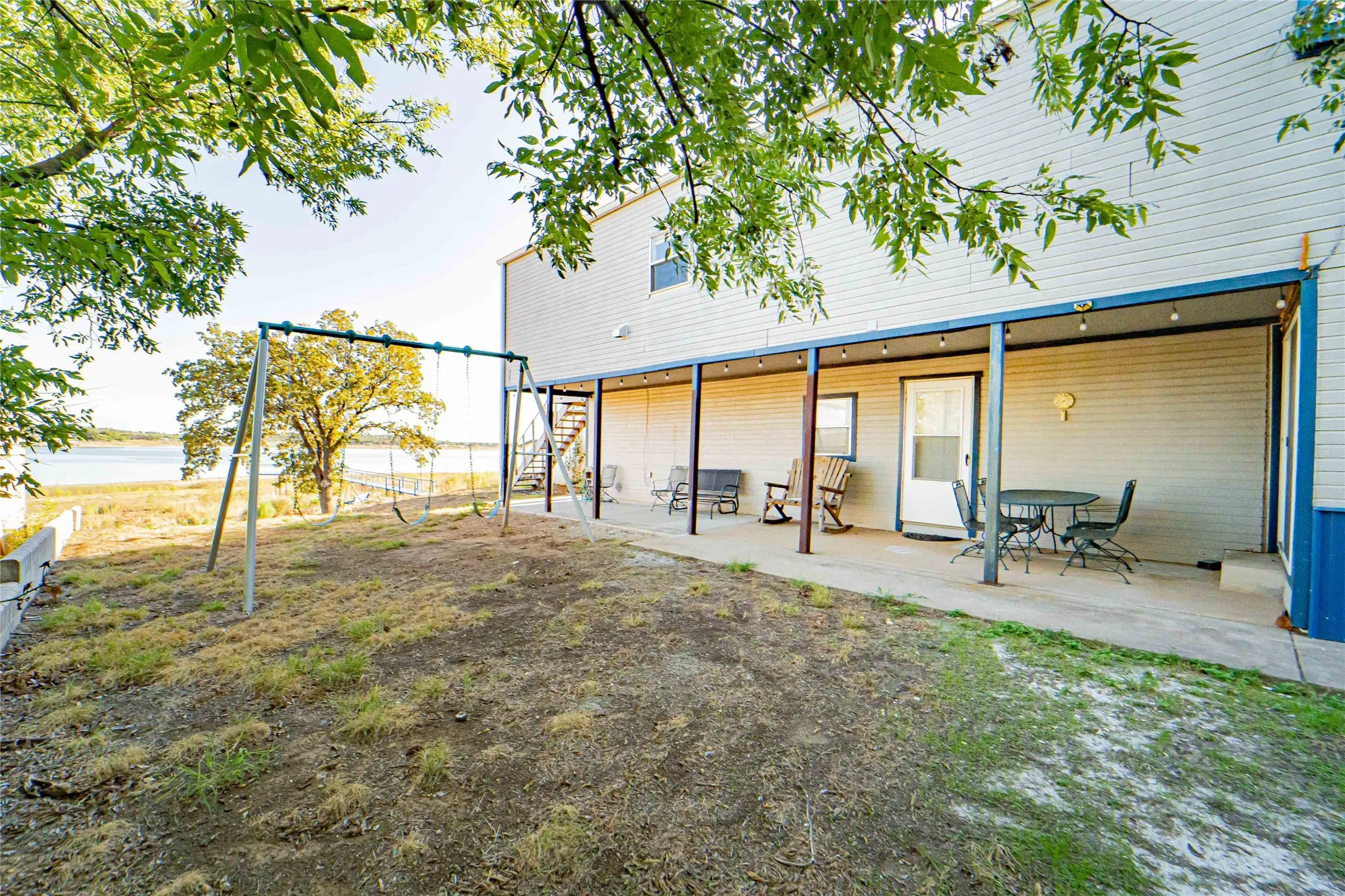 Expansive waterfront property featuring a covered patio, exterior staircase, and mature trees