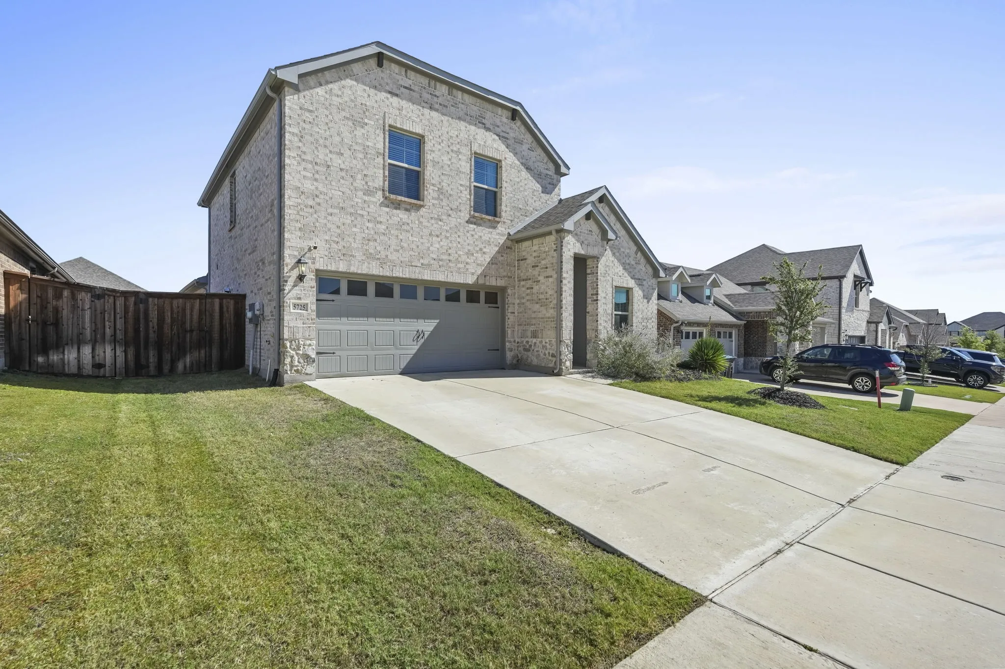 Brick exterior with a two-car garage, concrete driveway, and a wood privacy fence