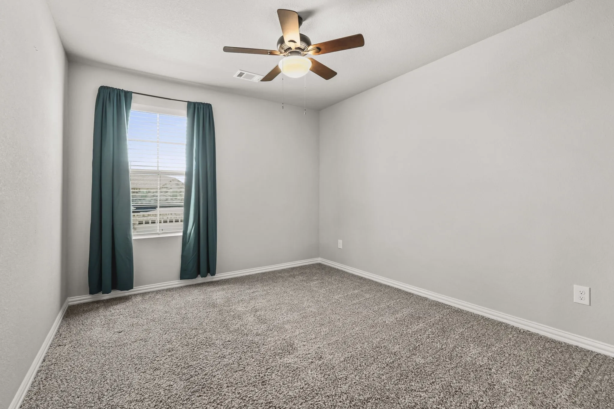 Neutral wall paint, textured carpeting, a single window with blinds, and a ceiling fan with integrated lighting