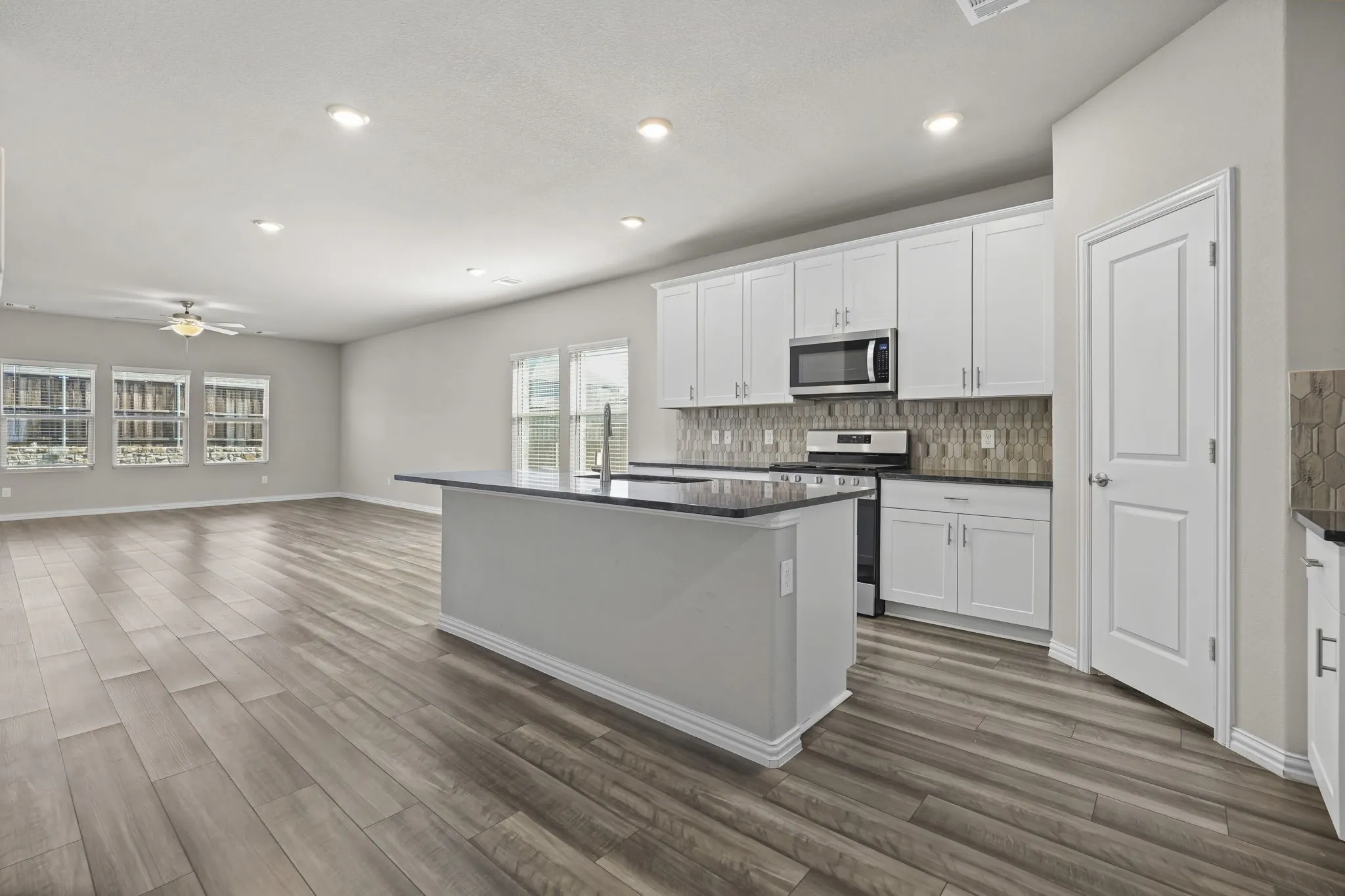 Kitchen island with dark countertop, stainless steel appliances, white cabinetry, and a tile backsplash