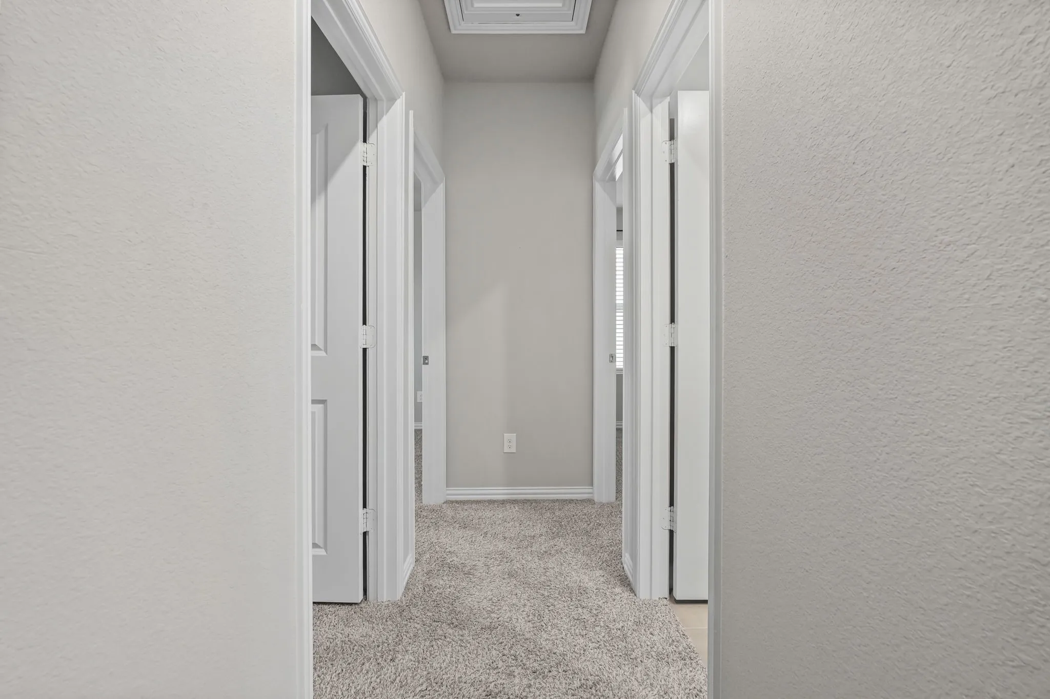 Hallway with light gray textured walls, white trim, and light gray carpeted flooring