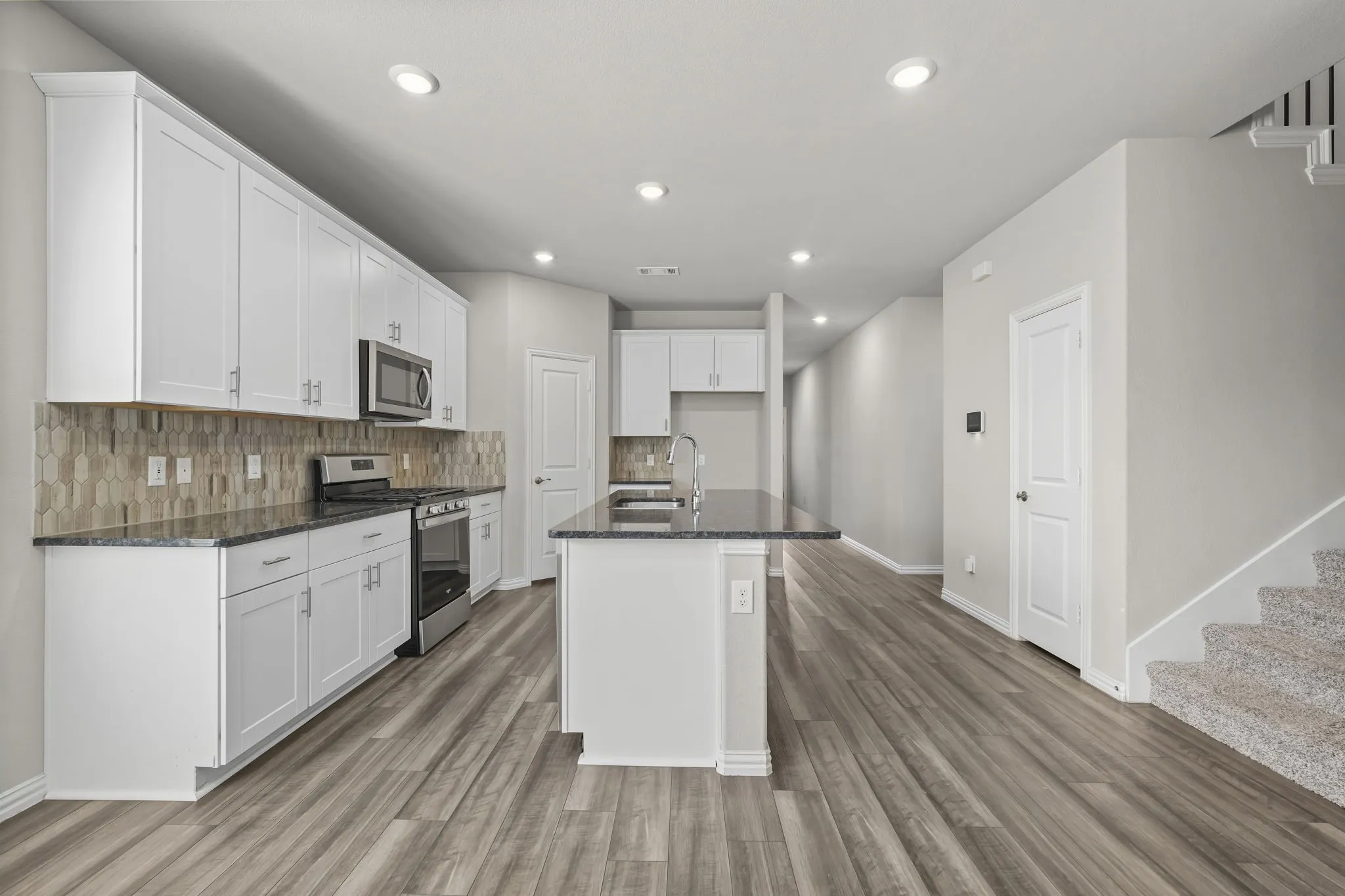 Kitchen featuring white cabinetry, dark countertops, stainless steel appliances, and a hexagonal tile backsplash